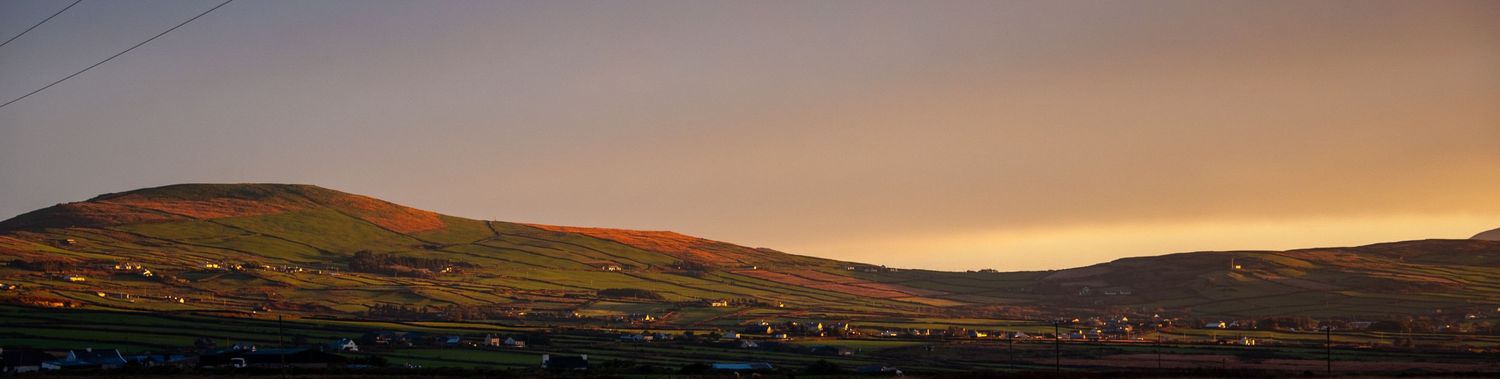 Ultra-wide panoramic landscape of hills and farmland under a dramatic evening sky.