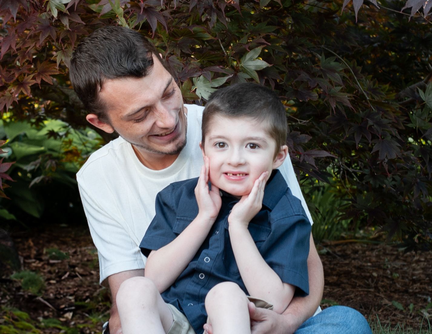 A tender family moment shared between a parent and child sitting together outdoors with autumn foliage in the background.