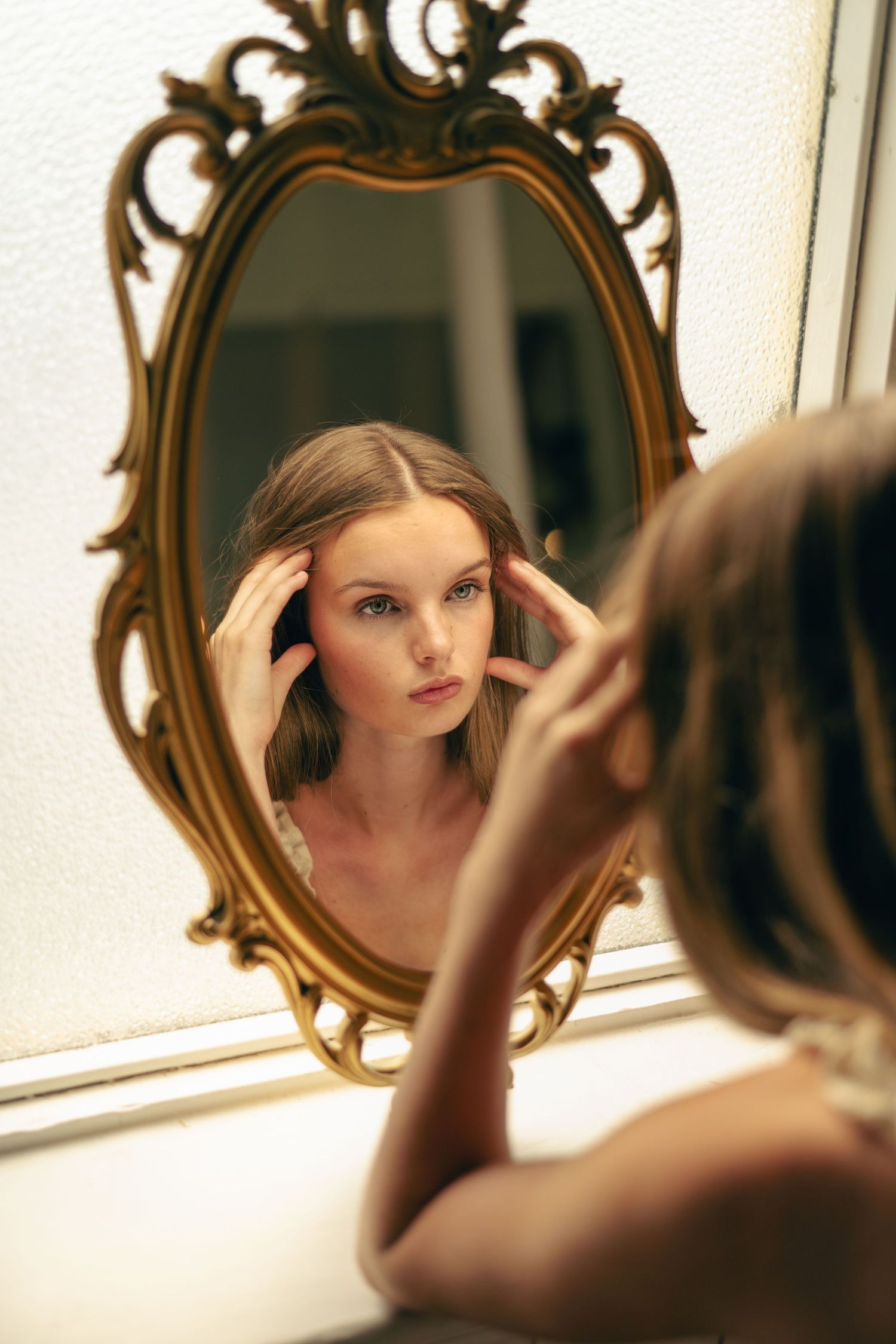 A hand adjusts hair while looking in an ornate gold-framed mirror, reflected in multiple mirror angles.