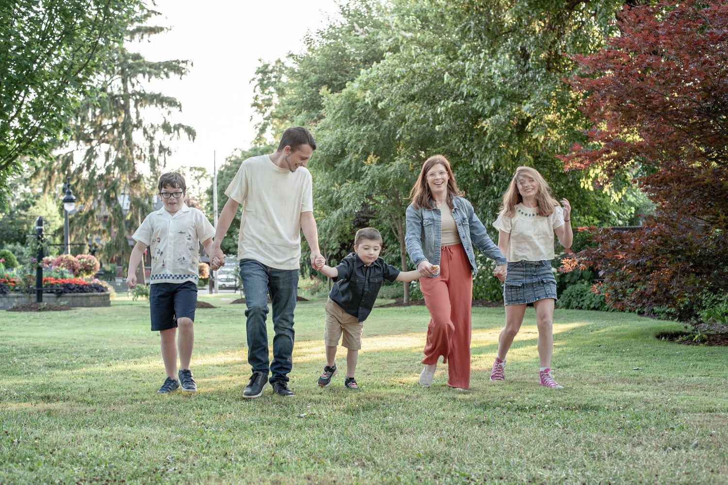 Large group enjoying a summer evening stroll through a lush green park area with trees in the background.