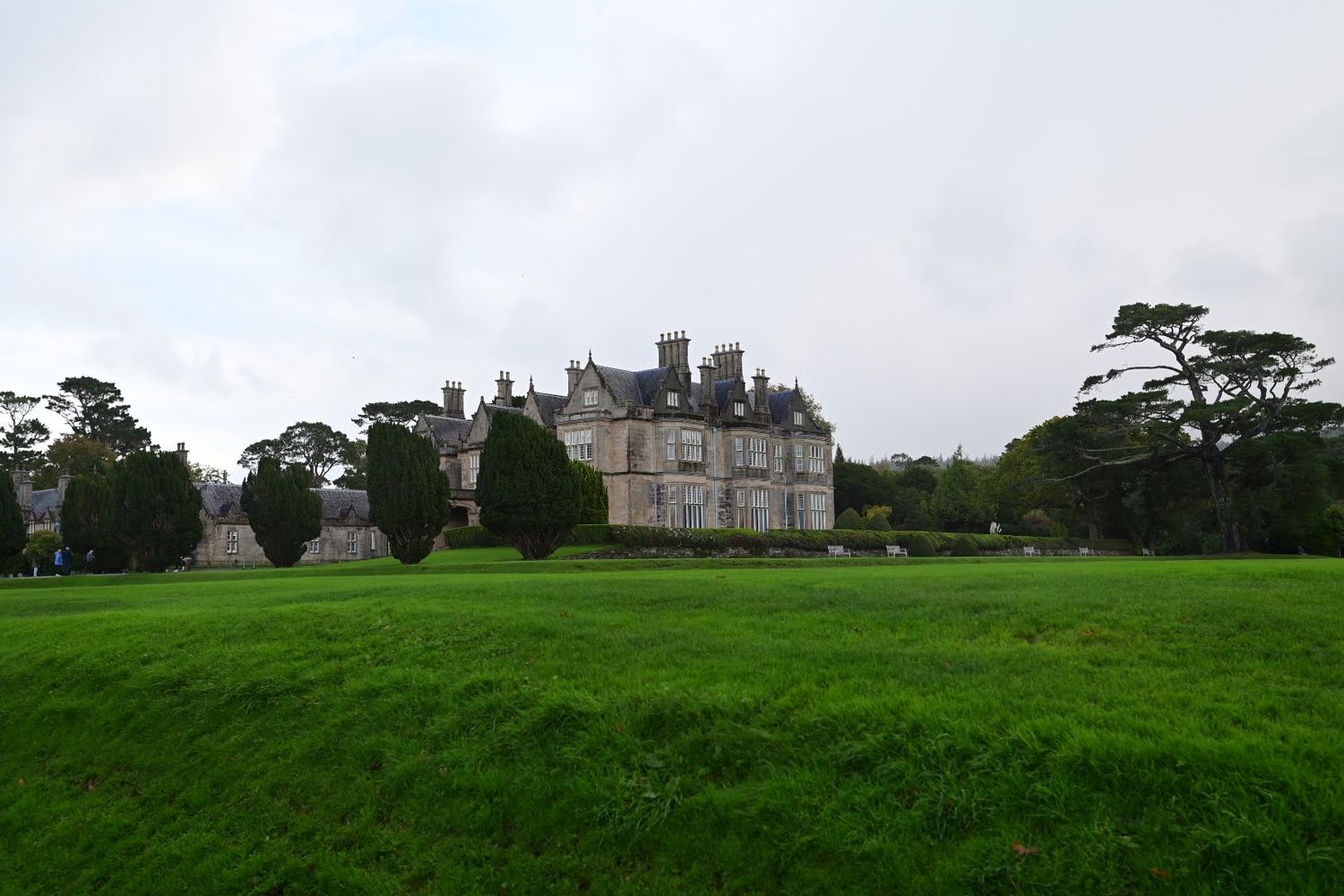 Historic stone mansion sits on expansive green lawn with mature trees in the background.