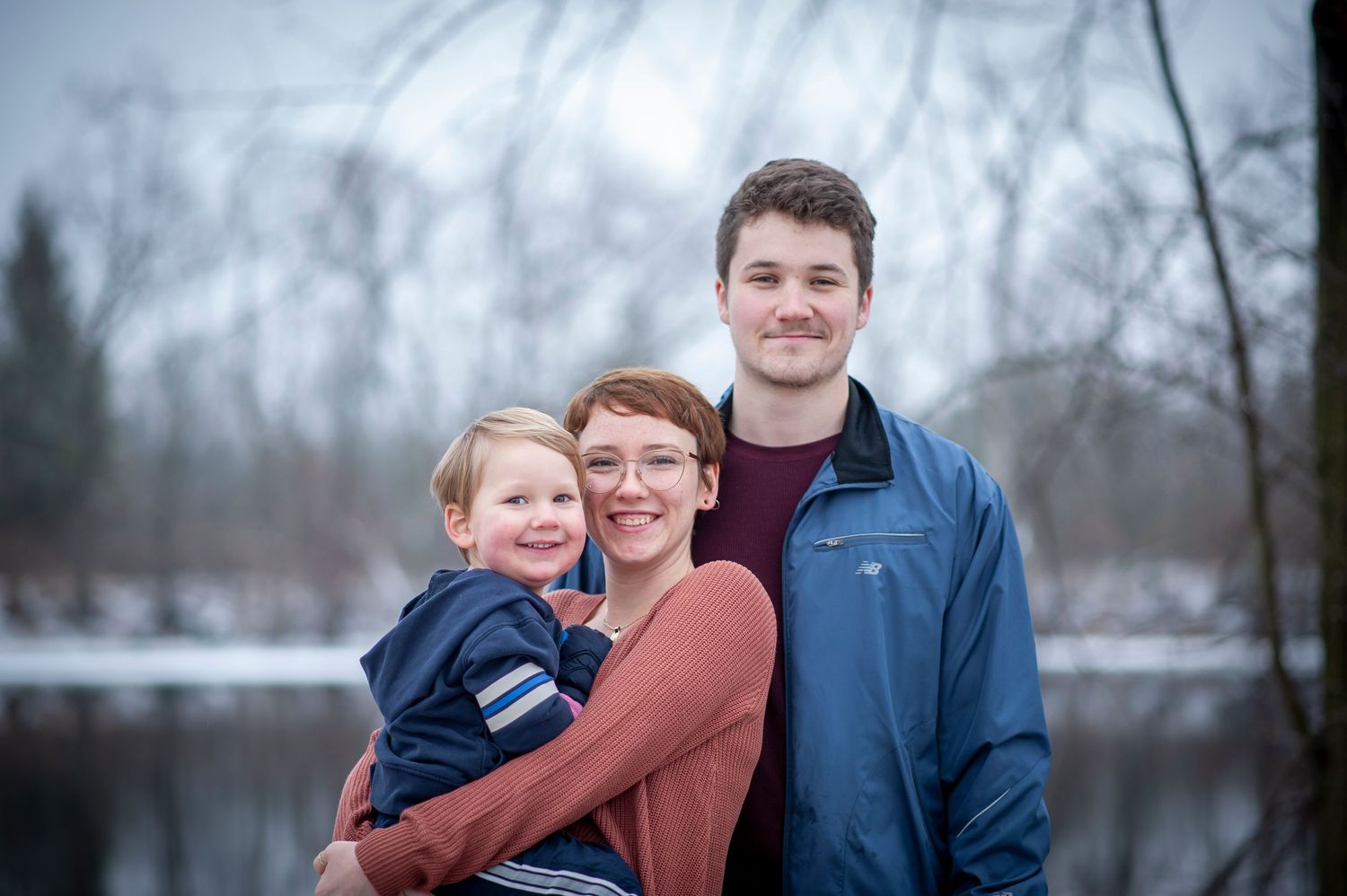 Winter family portrait by a lake with snowy landscape in background.