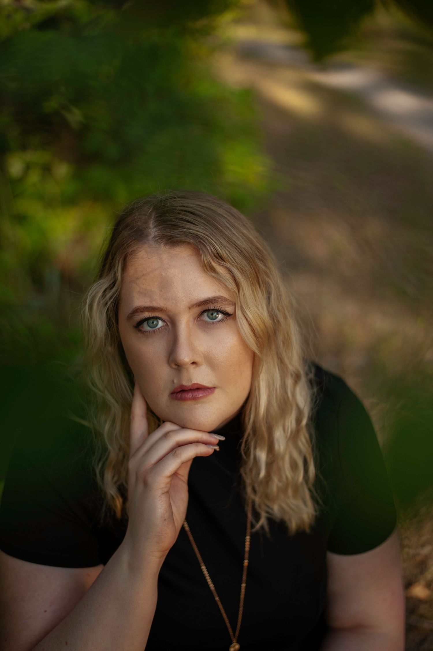 Portrait of a woman with wavy blonde hair in a black top against a blurred natural background.