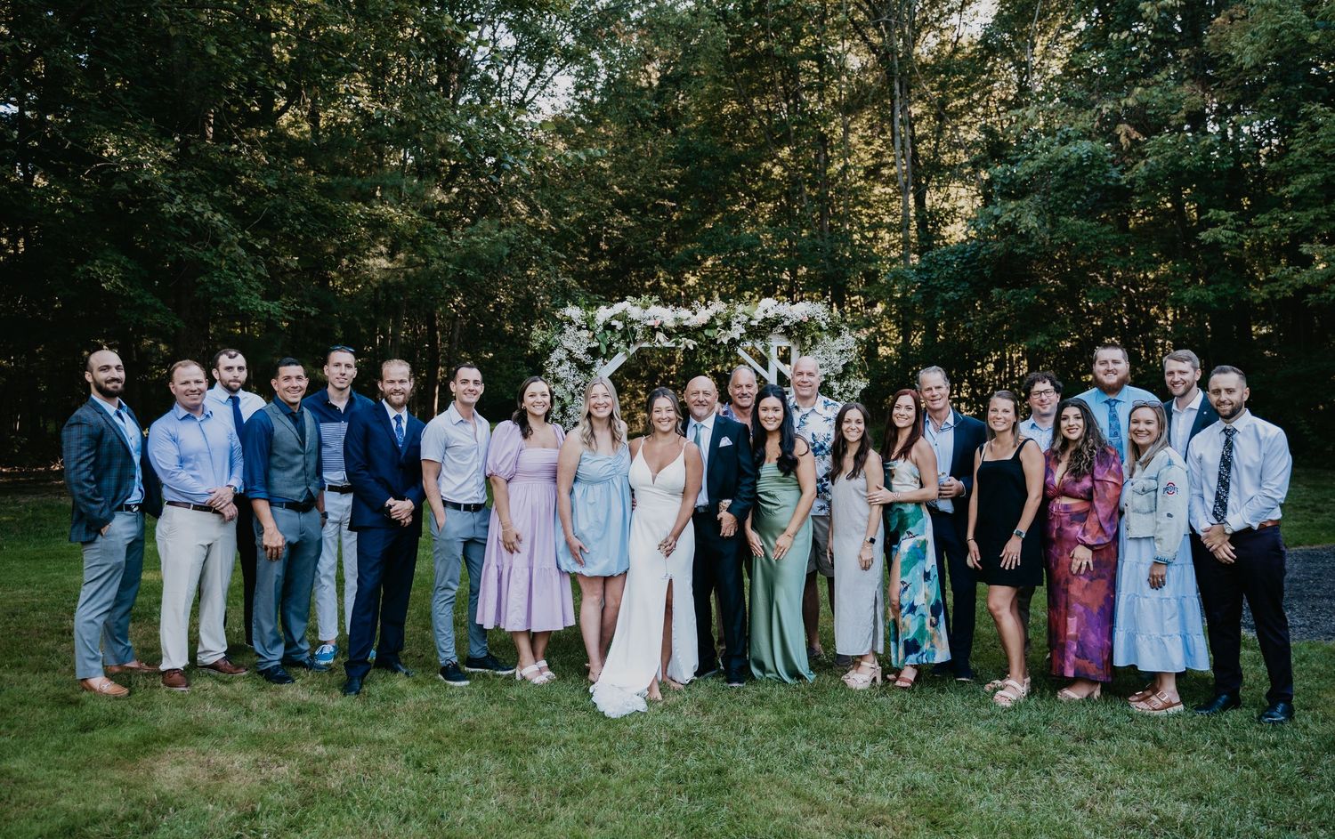 Wedding party members gather outdoors in coordinated pastel attire for group photos in a garden setting.