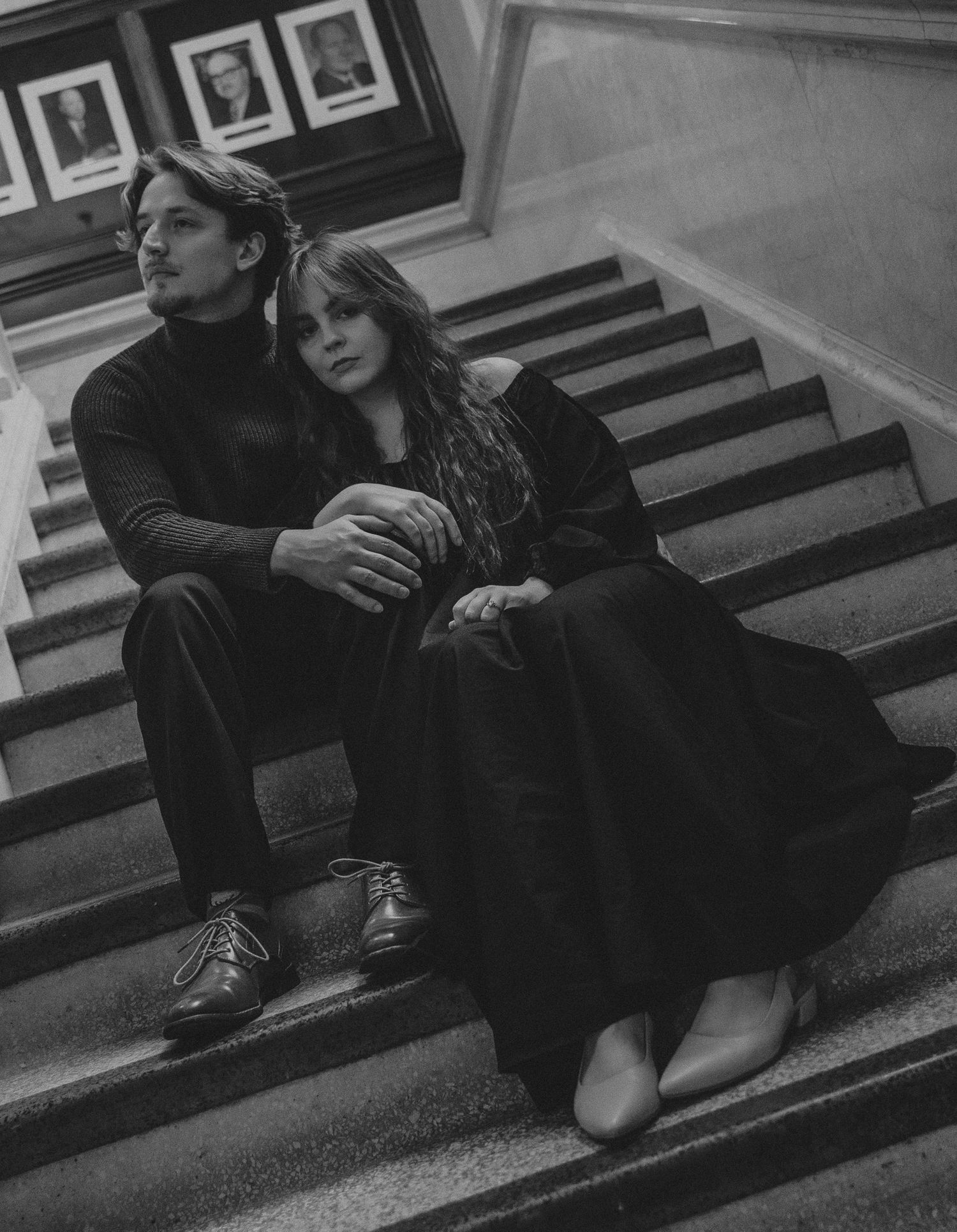 A black and white photo series showing a couple sitting intimately on wooden stairs with framed photos in background.