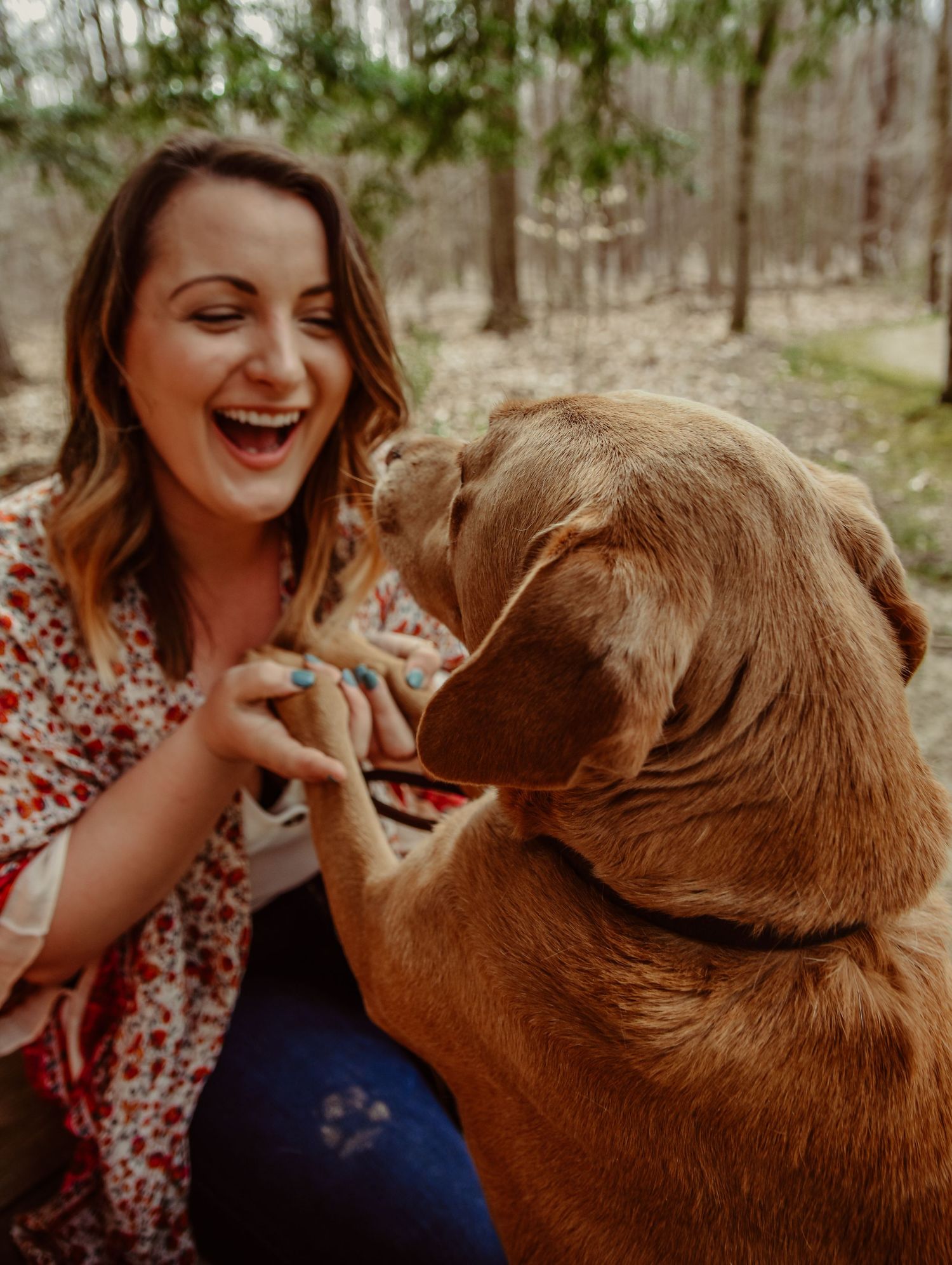 Woman laughing joyfully while playing with her golden retriever dog outdoors.