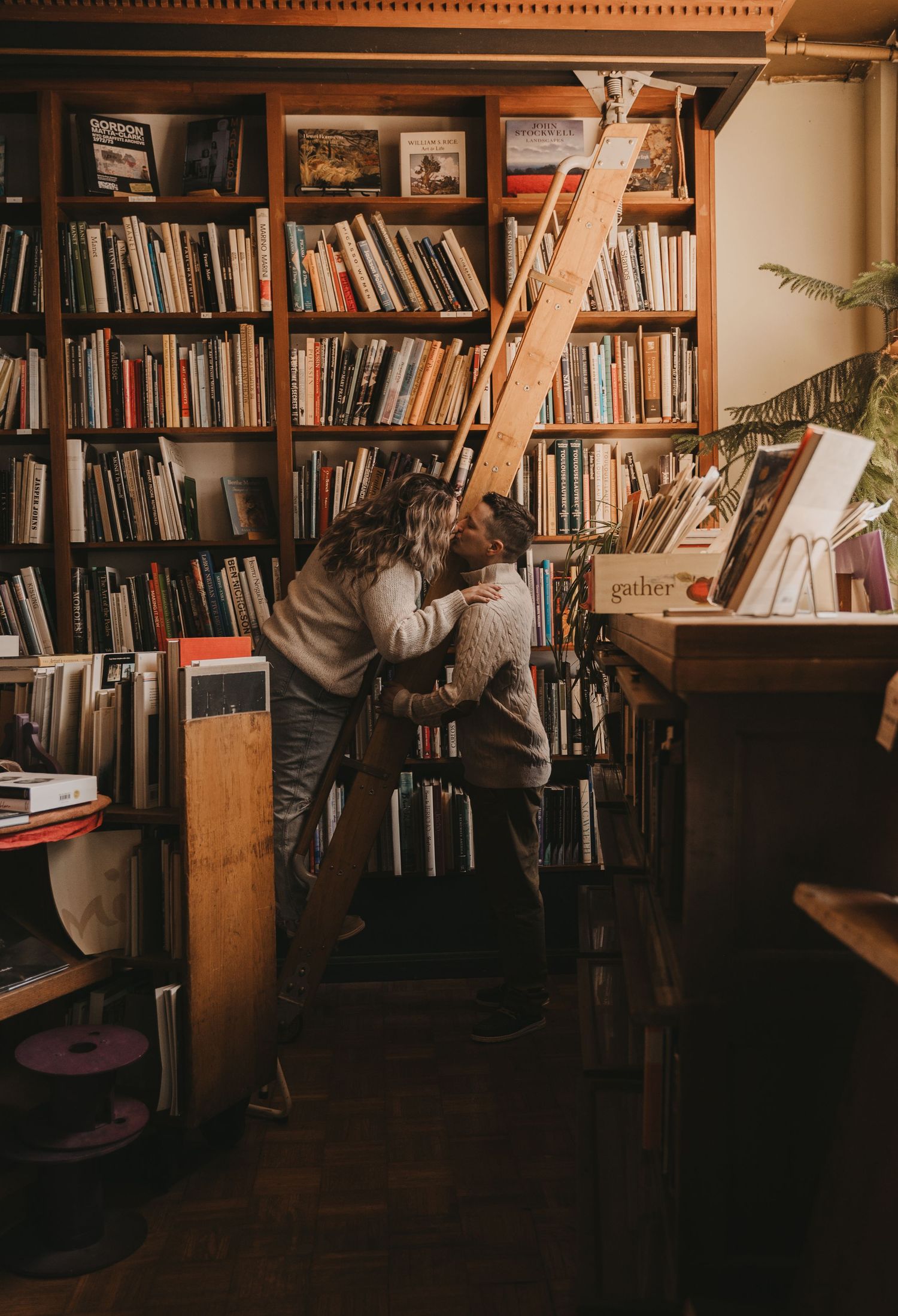 A cozy library interior with wooden bookshelves and a ladder against warm lighting creates an intimate reading atmosphere.