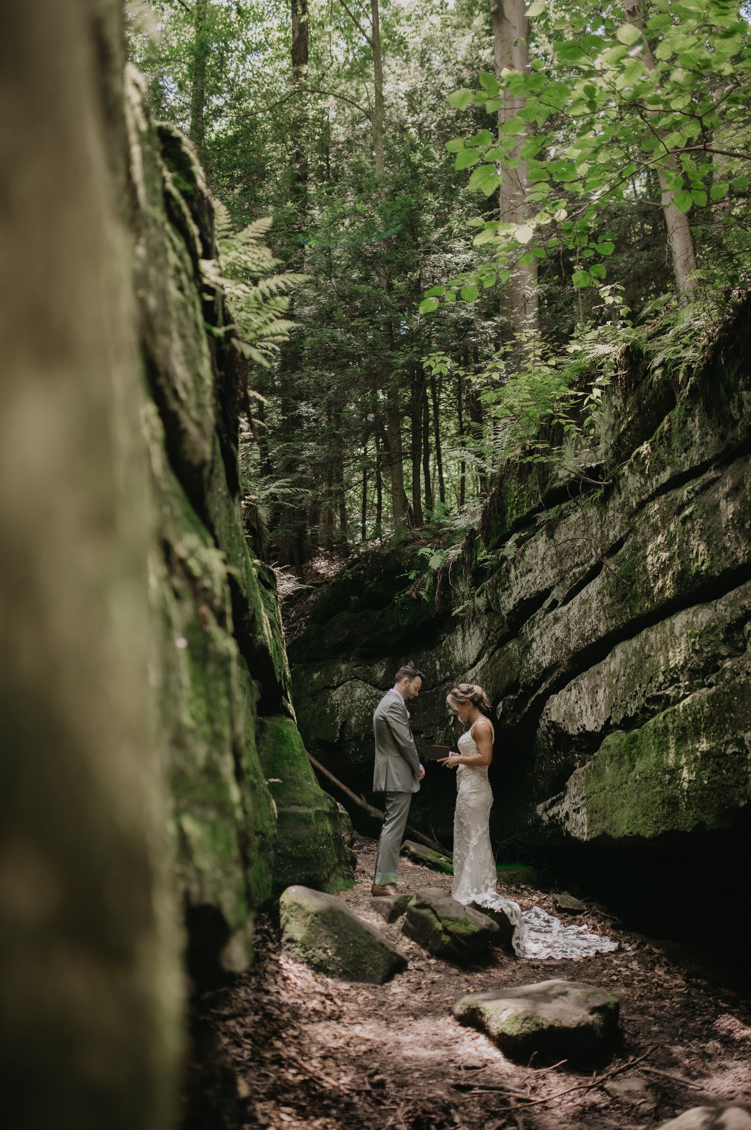 A couple stands together in a mossy forest canyon surrounded by towering rock walls and lush greenery.