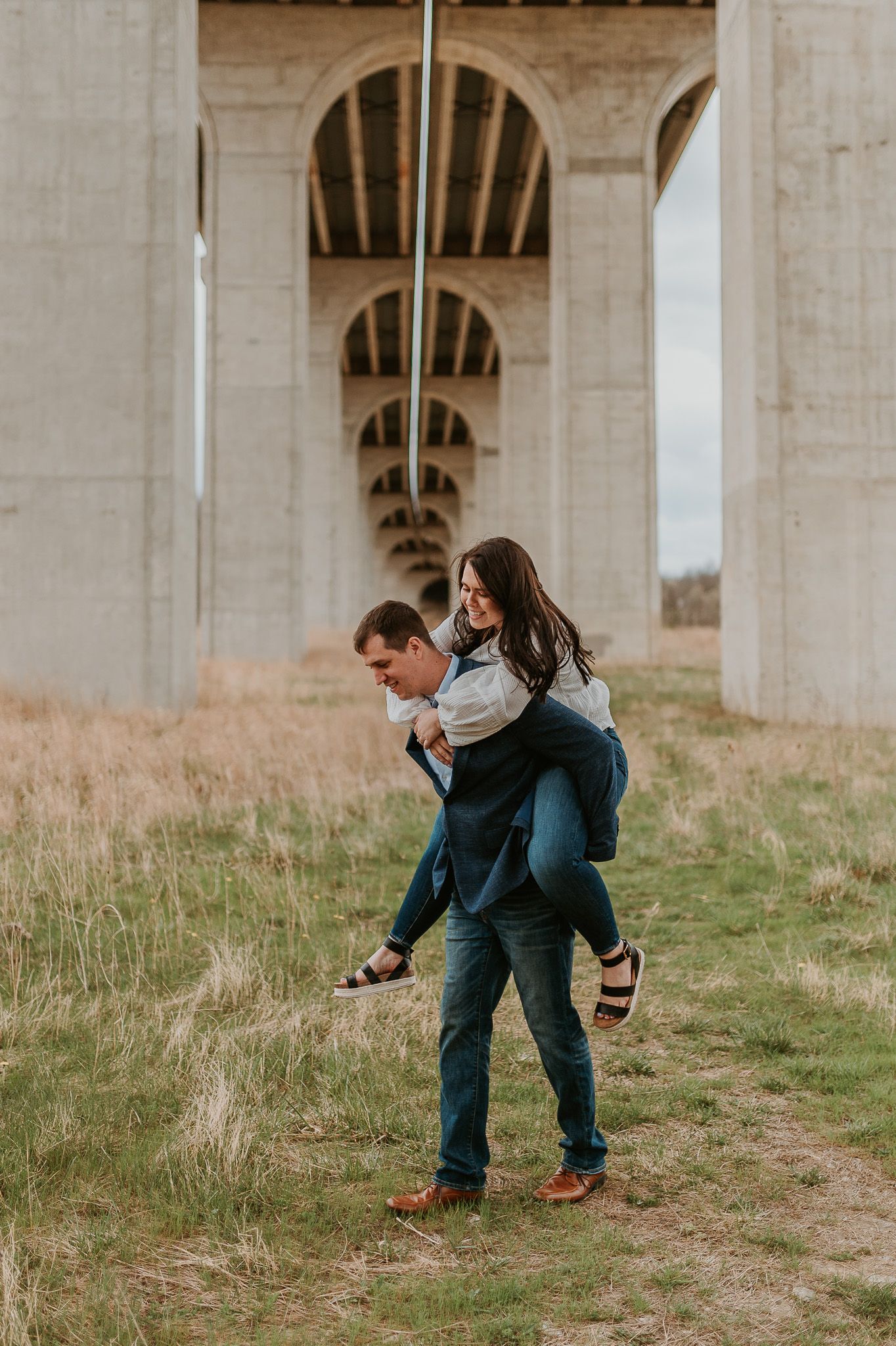 Playful couple sharing a sweet moment under concrete bridge pillars in a field.