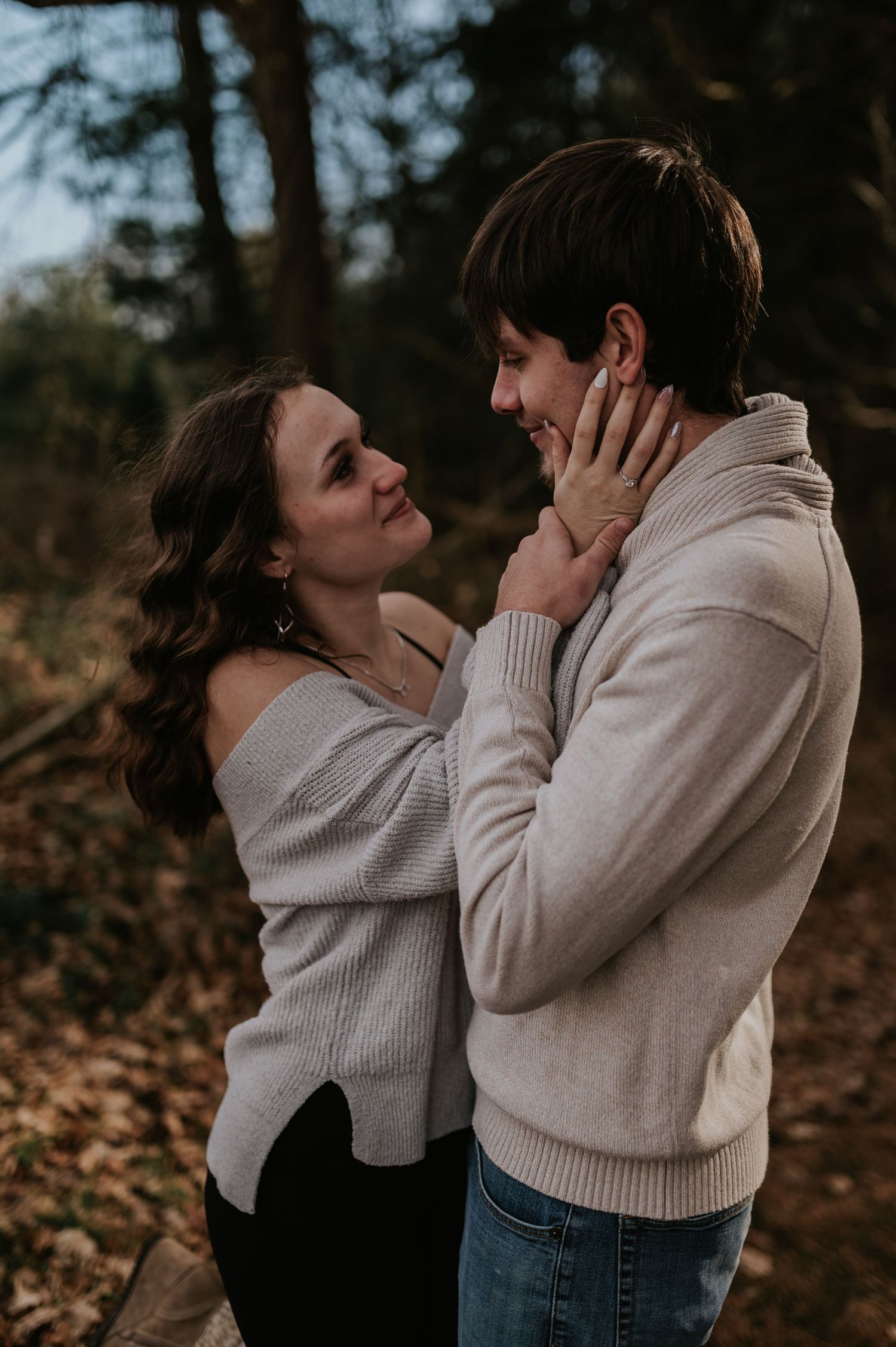 Couple in matching light sweaters sharing joyful moment in autumn woods.