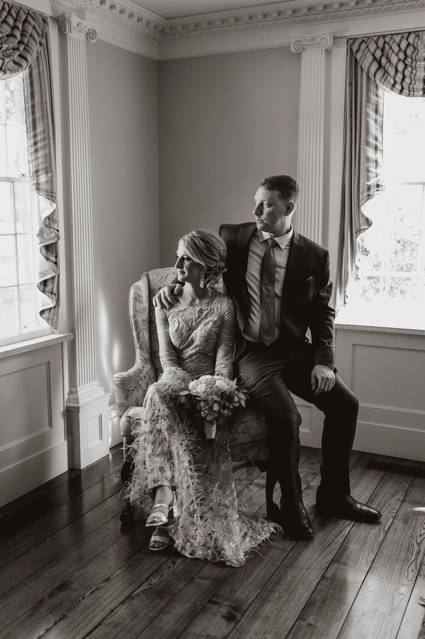 A romantic black and white wedding portrait taken in an elegant room with classic architectural details and windows.