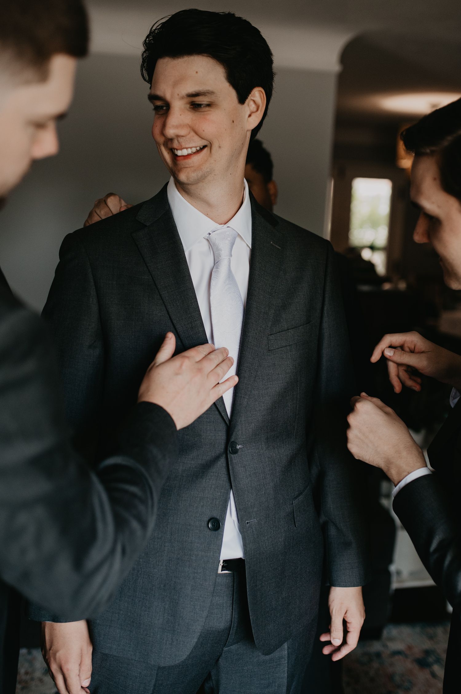 Groomsmen help each other get ready before a wedding ceremony, adjusting suits and ties in a candid moment.
