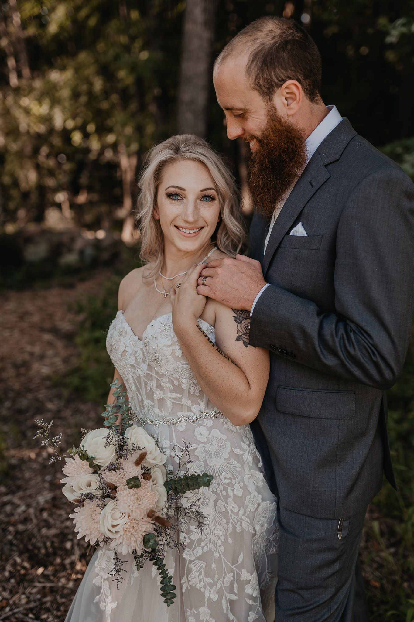 Happy couple in wedding attire pose together with bride holding elegant blush and white bouquet.
