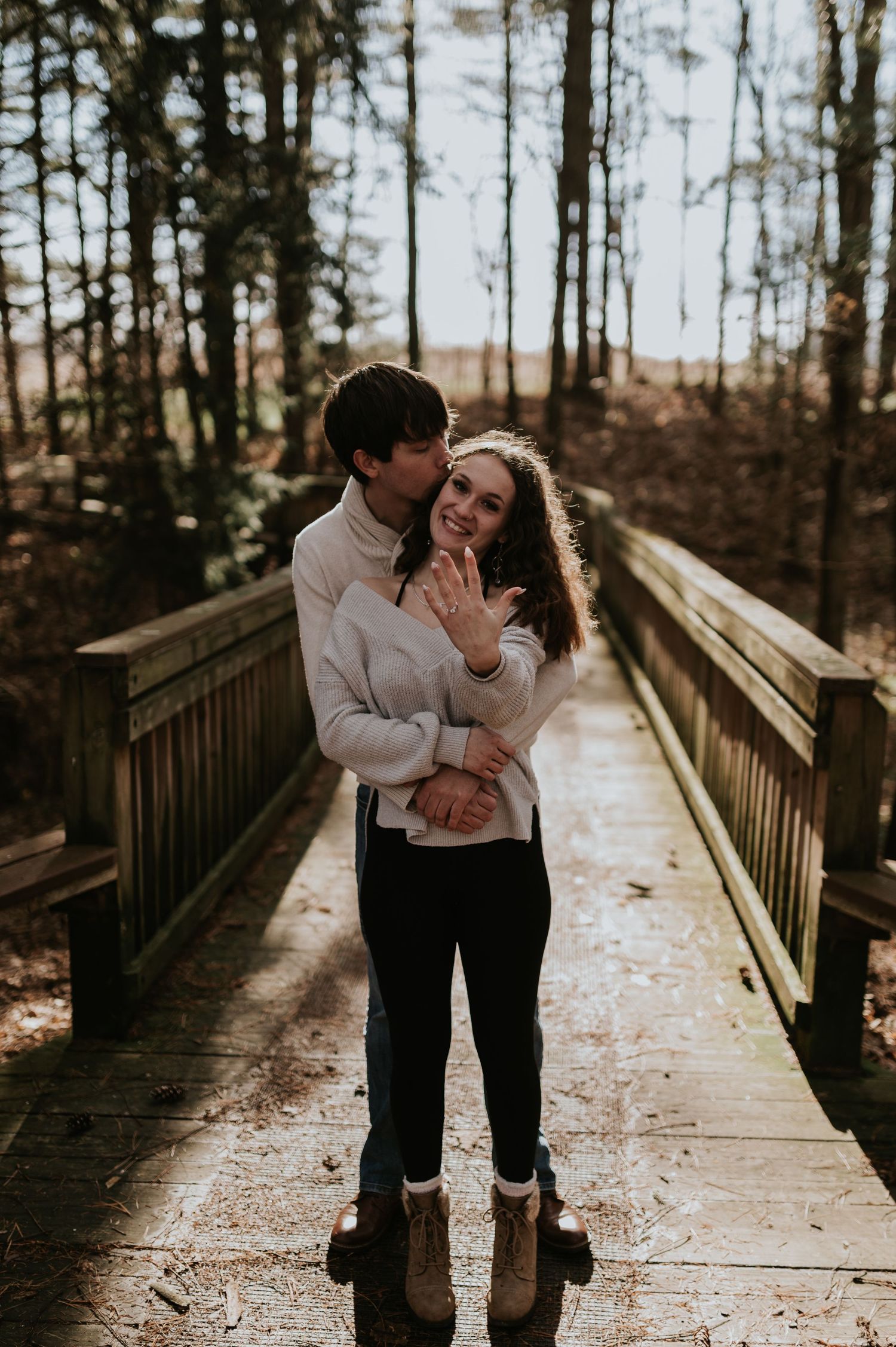 A couple embracing on a wooden walkway surrounded by winter trees.