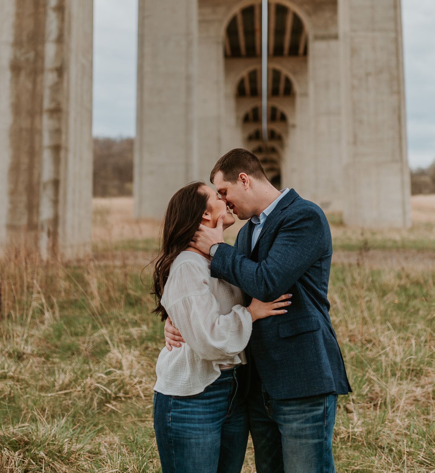 A romantic photoshoot under stone architecture with someone in a navy suit and light colored top sharing an intimate moment.