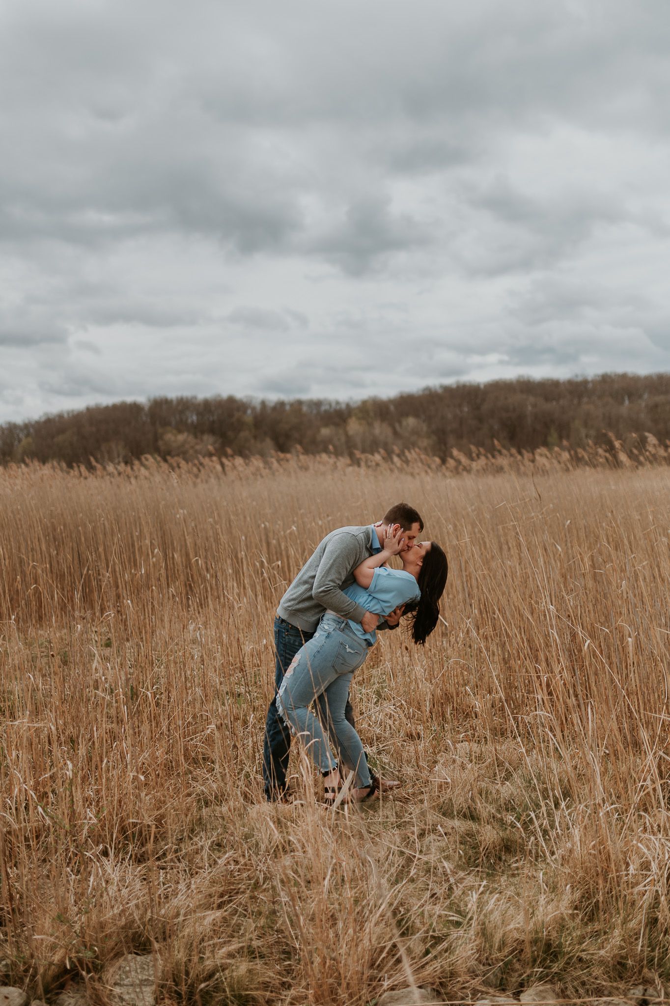 A romantic dip pose in a golden brown field under cloudy skies.