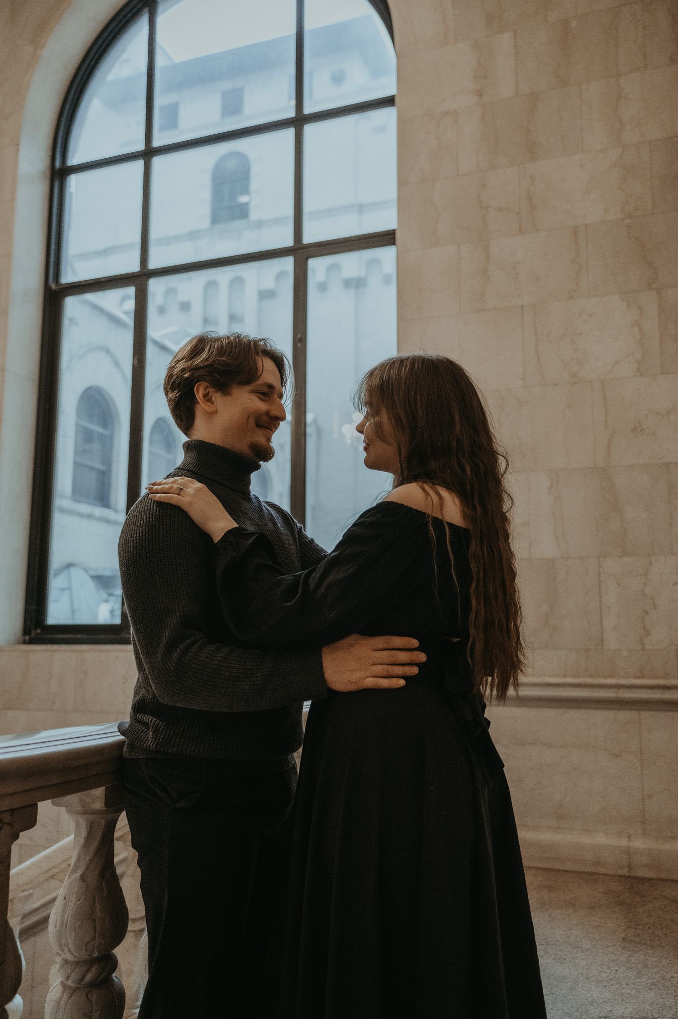 A couple shares intimate moments in a minimalist indoor space with large windows and natural light.