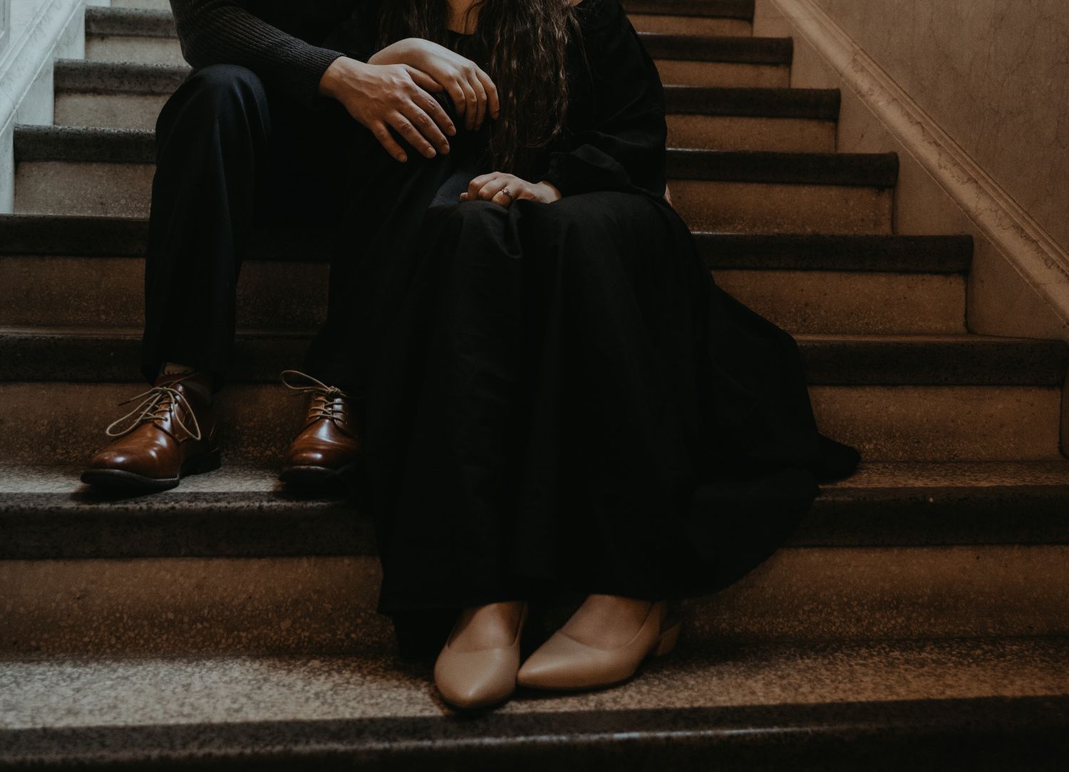 Feet of a person sitting on wooden stairs in a dark moody setting.