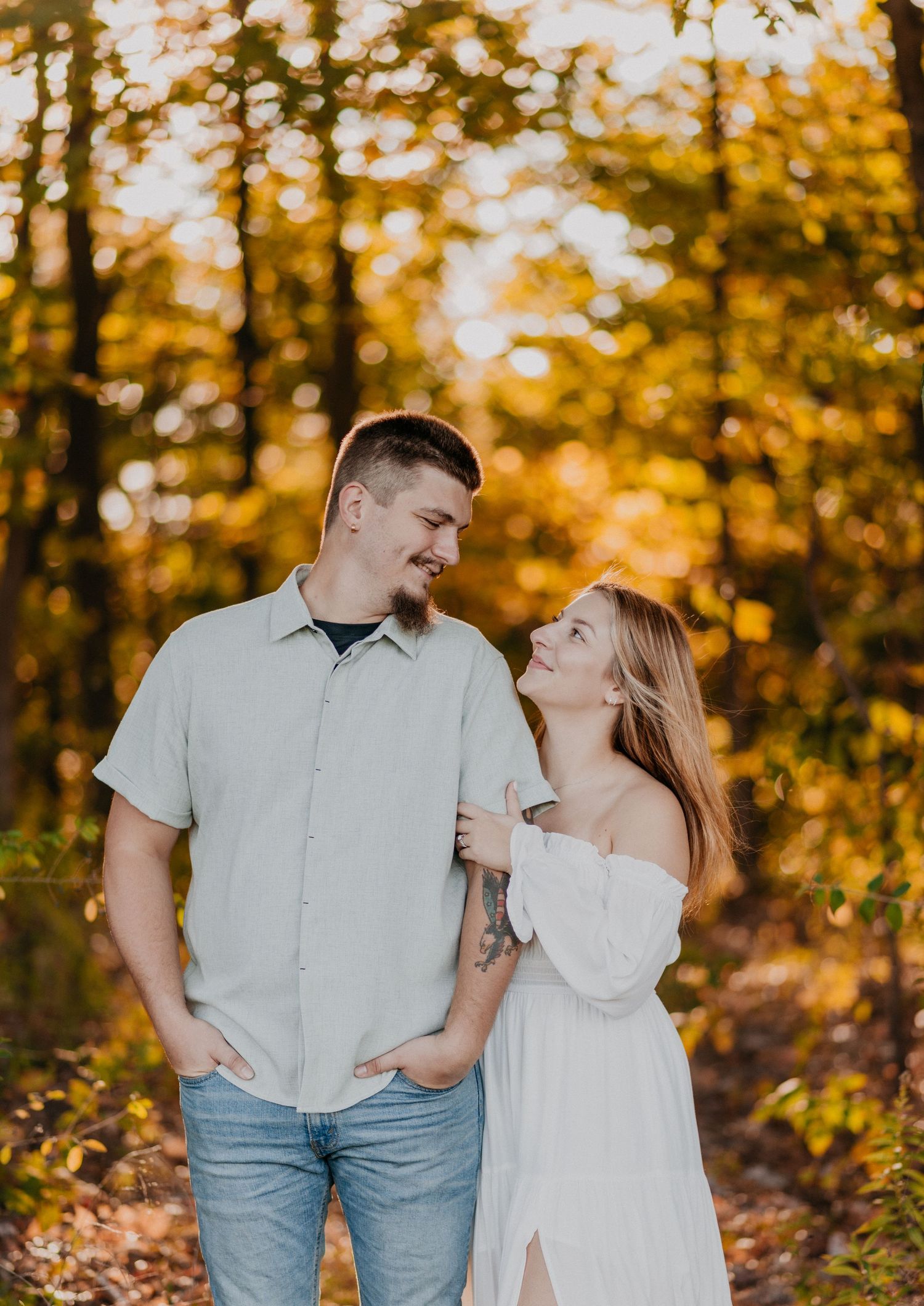 Couple shares a tender moment while walking through a wooded area with fall foliage.
