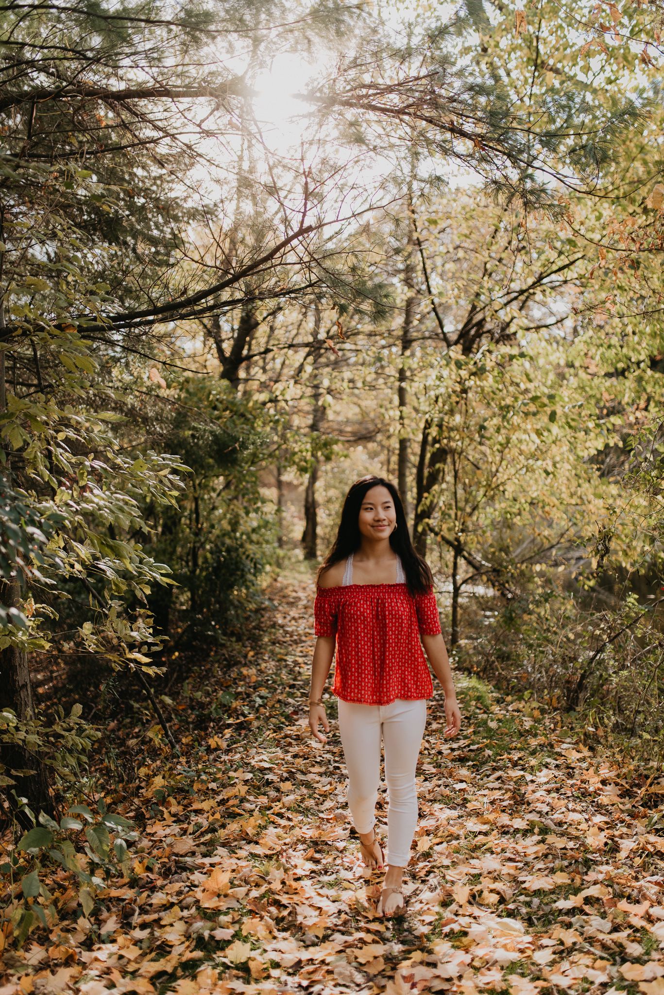 Autumn forest portrait wearing red off-shoulder top on leaf-covered path.