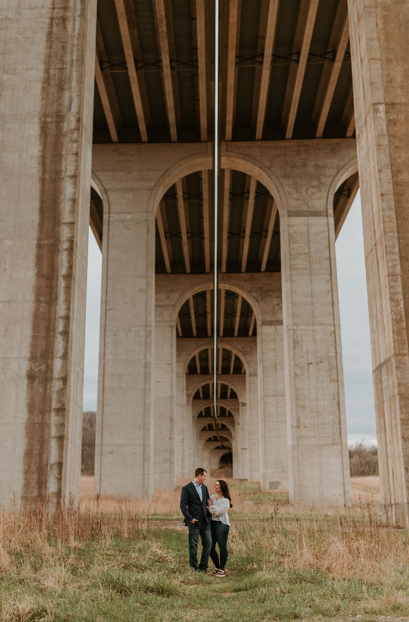 An engaged couple standing beneath massive concrete bridge arches during their photoshoot.