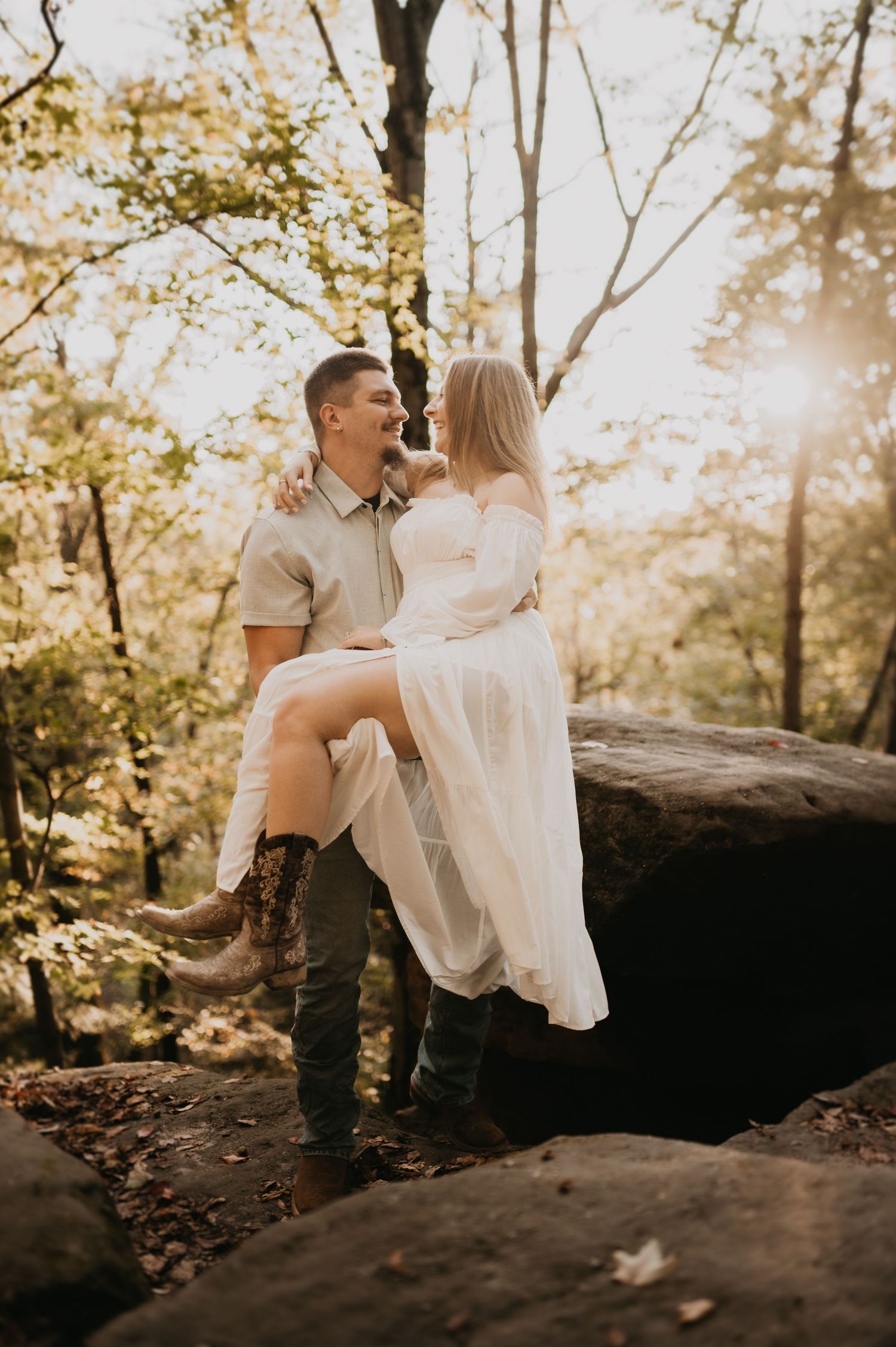 Couple sits together on rocky outcrop during golden hour photoshoot in nature.