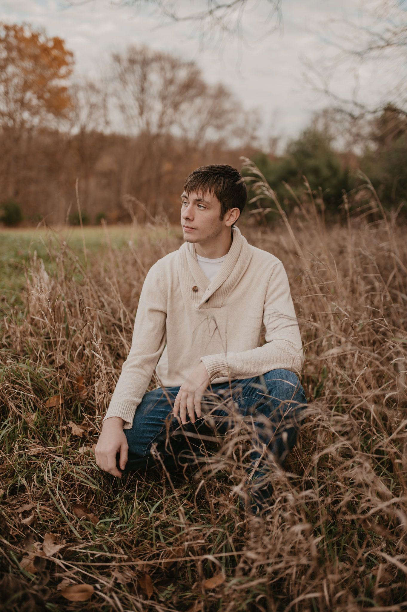 Someone poses in dried grass wearing a cream sweater during golden hour.