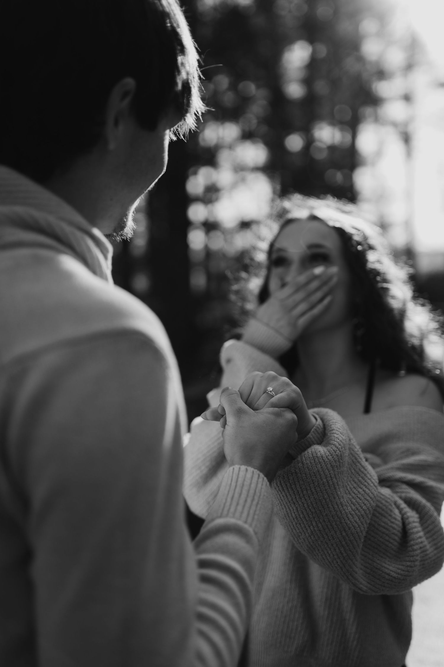 Black and white photo capturing an emotional reaction during an intimate forest proposal moment.