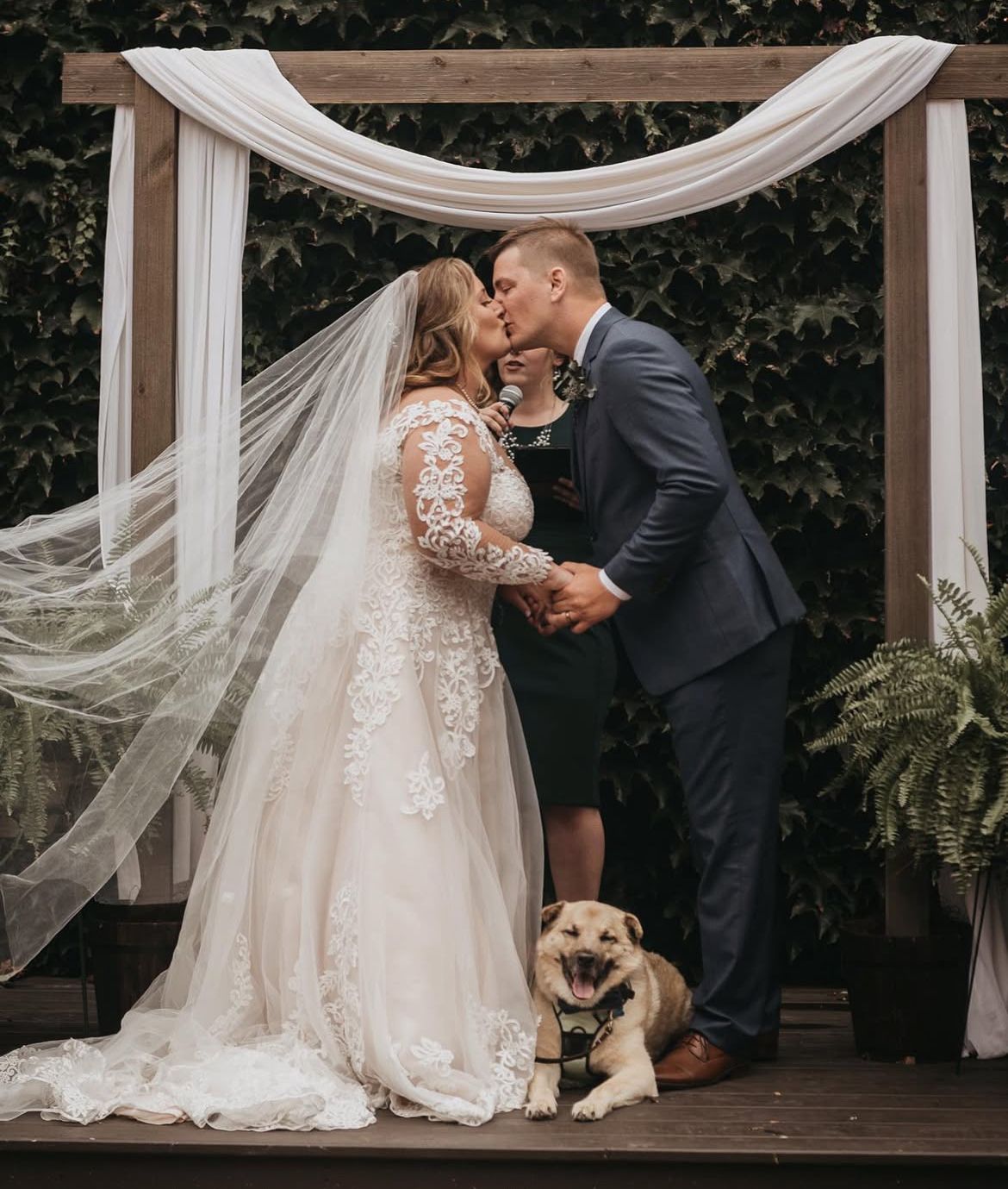 Wedding ceremony sequence showing couple sharing romantic kiss under white fabric draped archway.