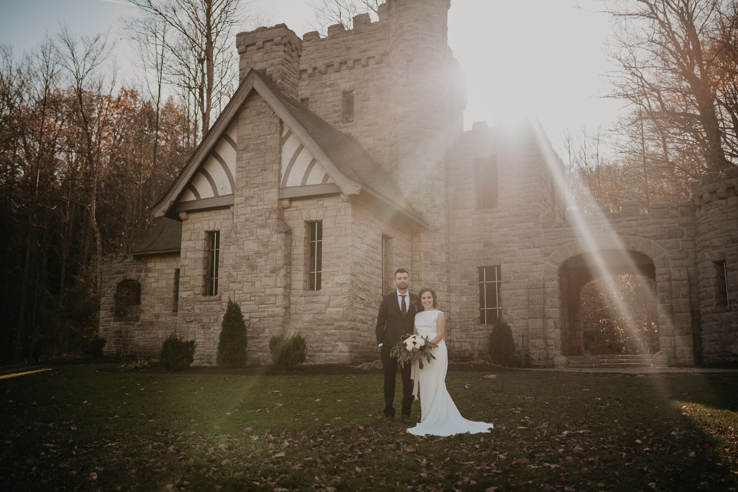 Wedding couple photographed against historic stone church with dramatic sunlight and landscape.