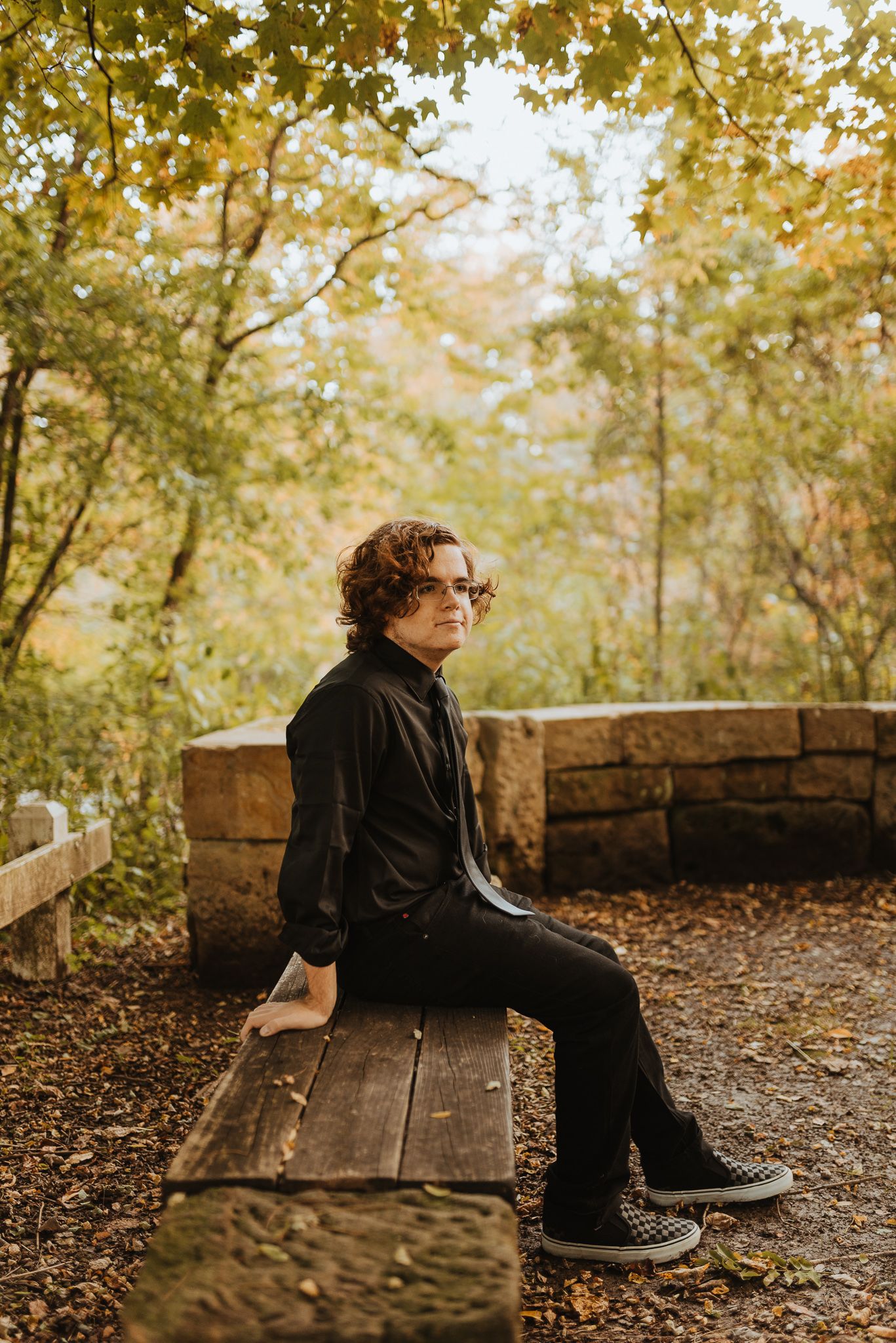 Person in black turtleneck sitting on wooden bench in autumn forest setting.