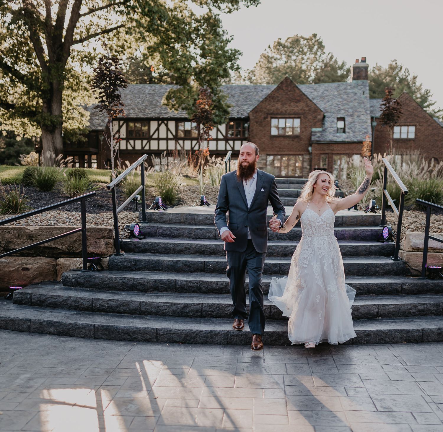 Newlyweds descend stone steps in front of Tudor-style wedding venue.