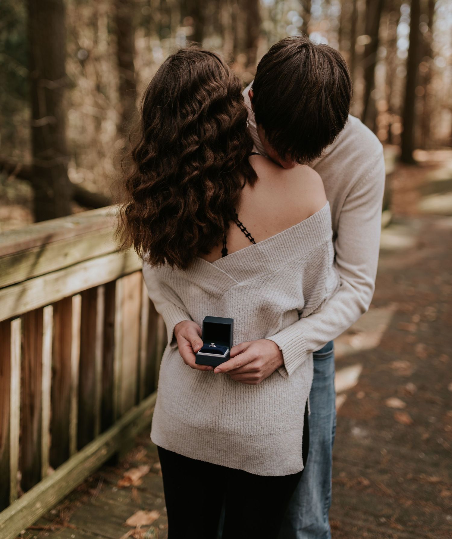 A couple embracing on a wooden boardwalk while holding a small box.