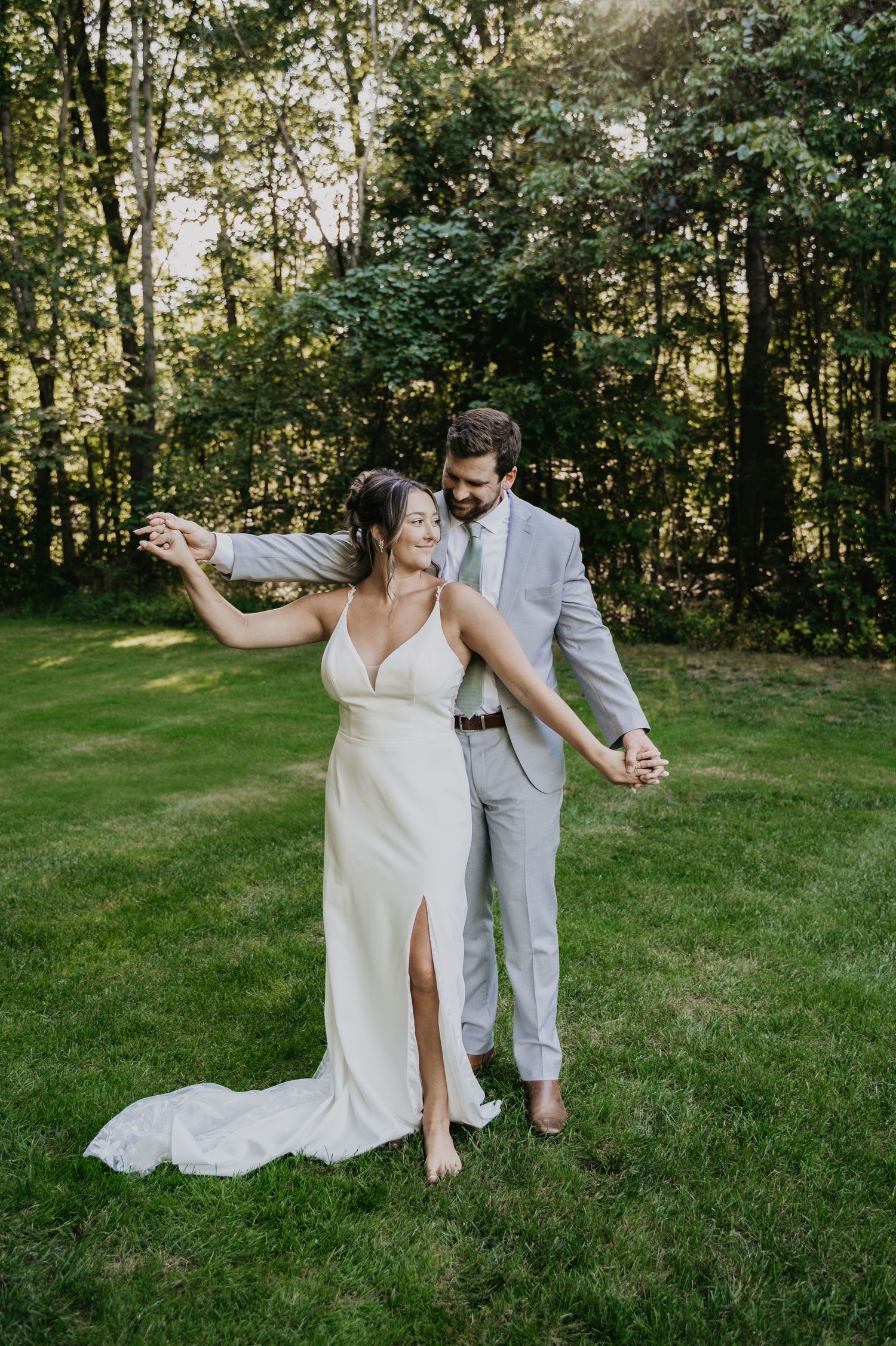 A couple dances joyfully on a green lawn during their outdoor wedding celebration.
