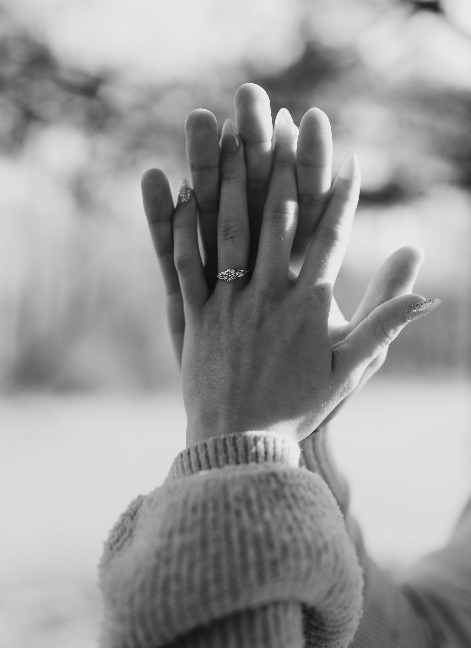 Black and white close-up of two hands displaying an engagement ring.