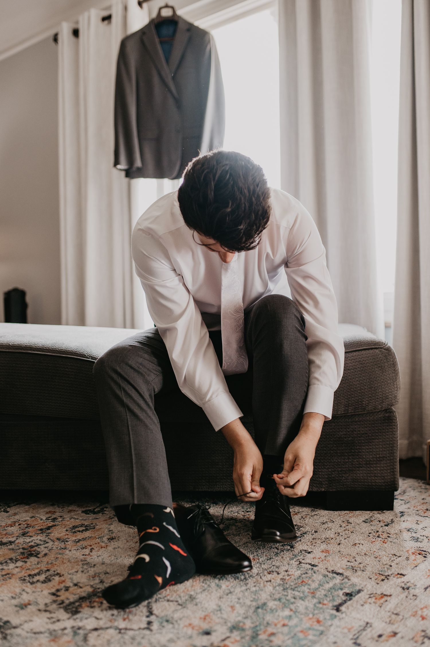 Close-up sequence showing hands tying dress shoes while sitting on dark couch with patterned carpet below.