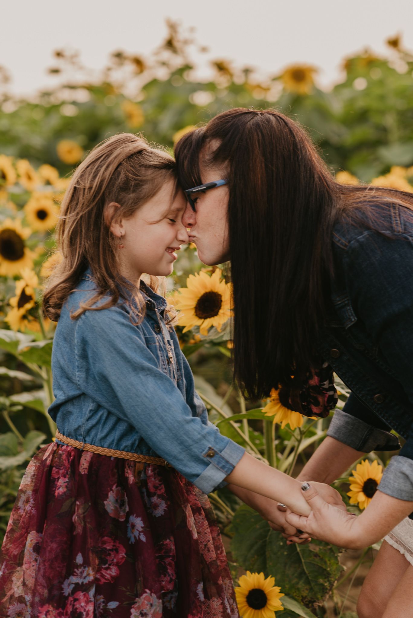 Mother and daughter touching noses affectionately in sunflower field.