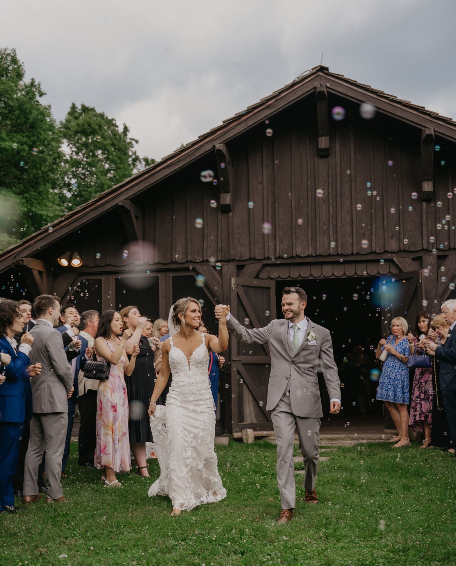 Wedding celebration outside rustic wooden barn with string lights and guests enjoying festivities.