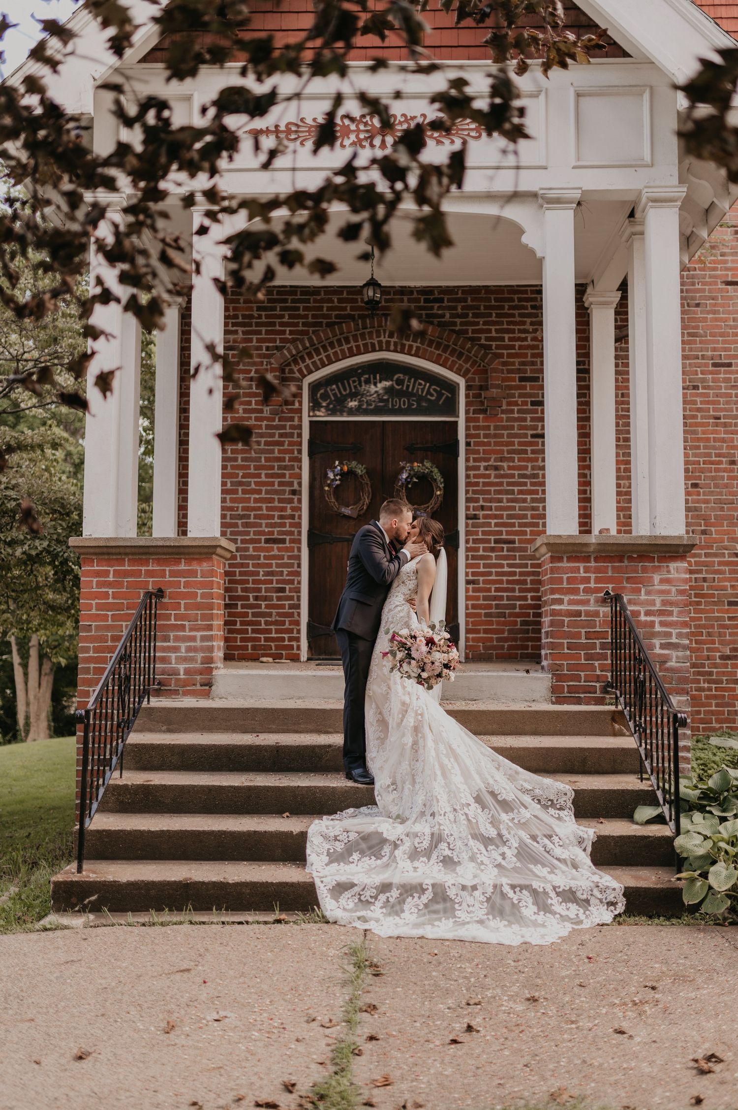 Romantic wedding photos in front of a brick church entrance featuring a long flowing lace veil.