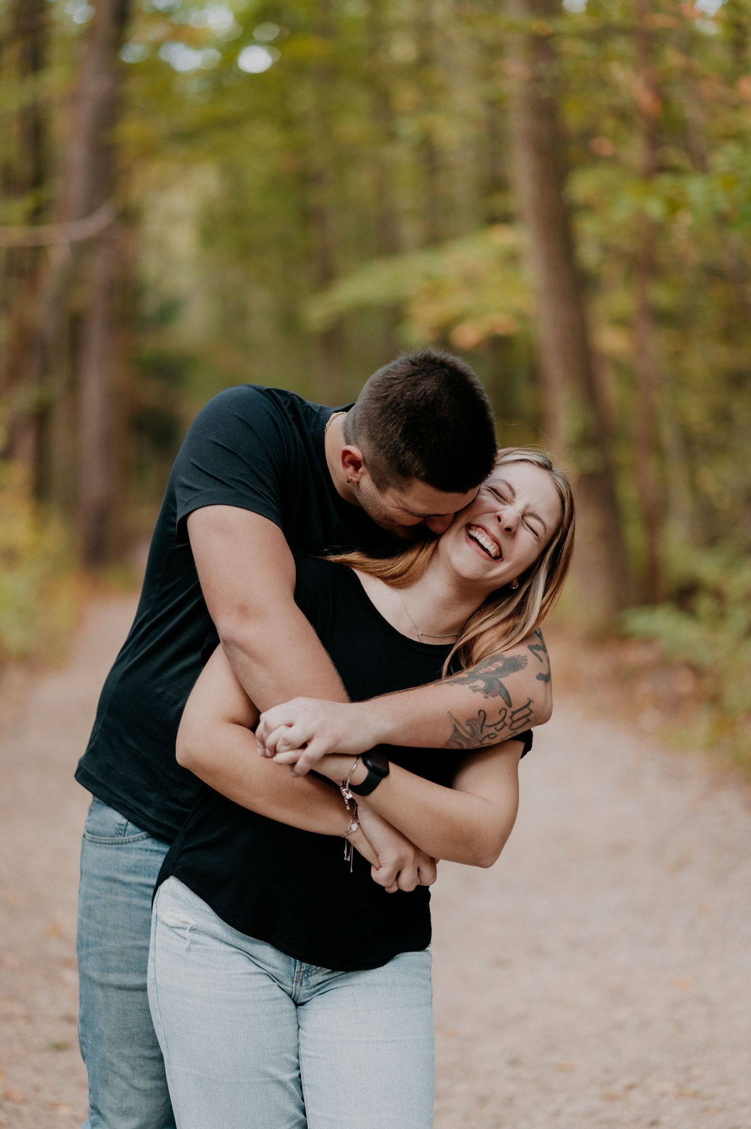 A couple shares an intimate moment on a forest path during an autumn day.