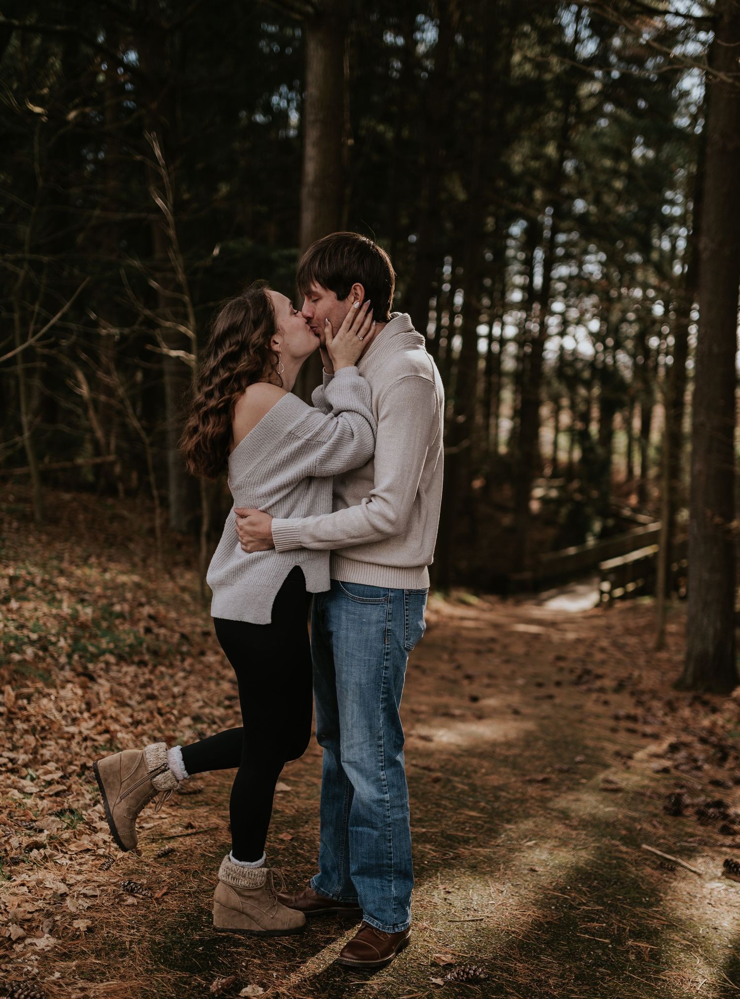 Romantic couple sharing an intimate kiss on a wooded trail during autumn.