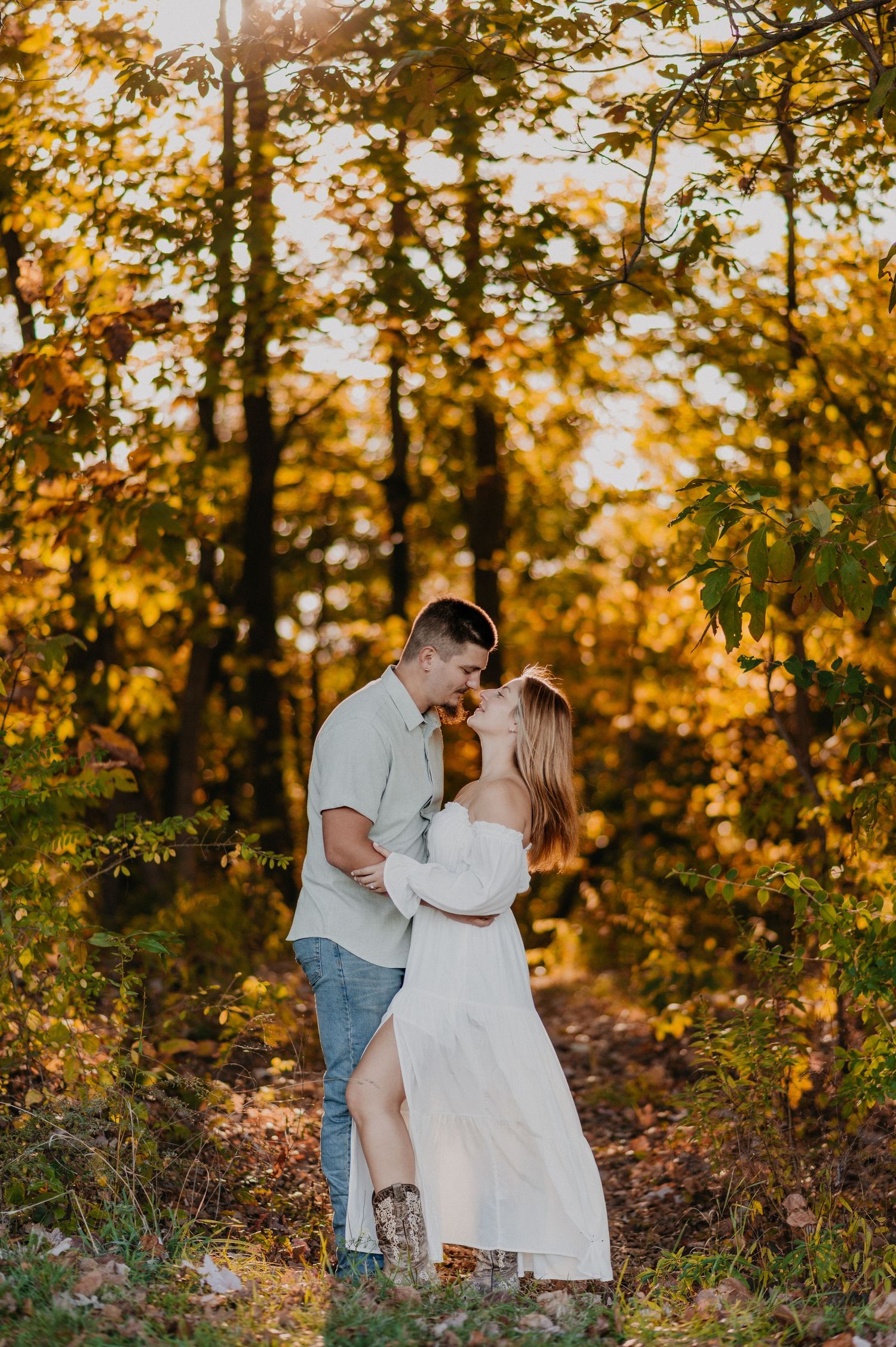 Romantic couple embraces in a sunlit autumn forest with golden leaves and warm lighting.