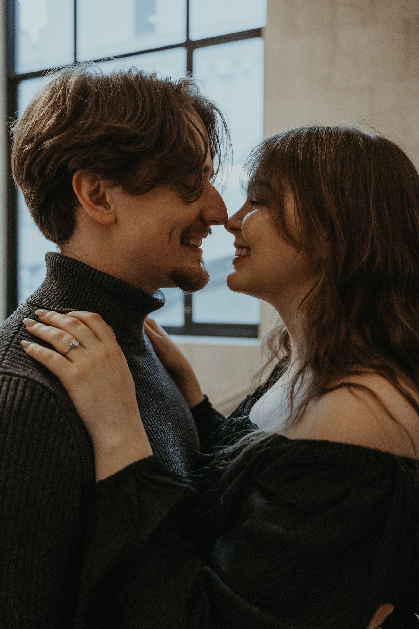 A romantic couple in dark sweaters share intimate moments in a sequence of black and white photos by a window.