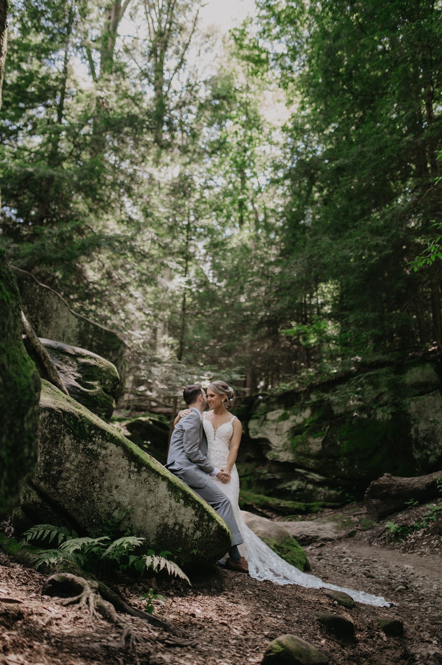 Newlyweds share tender moments along a wooded trail surrounded by lush greenery.