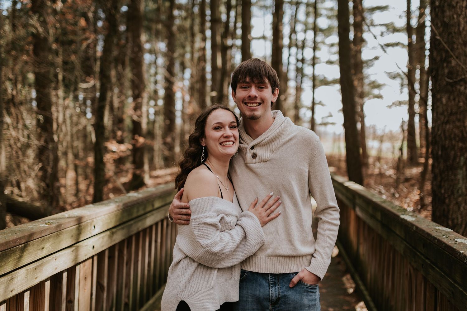 A happy couple sharing laughter on a wooden boardwalk surrounded by pine trees.
