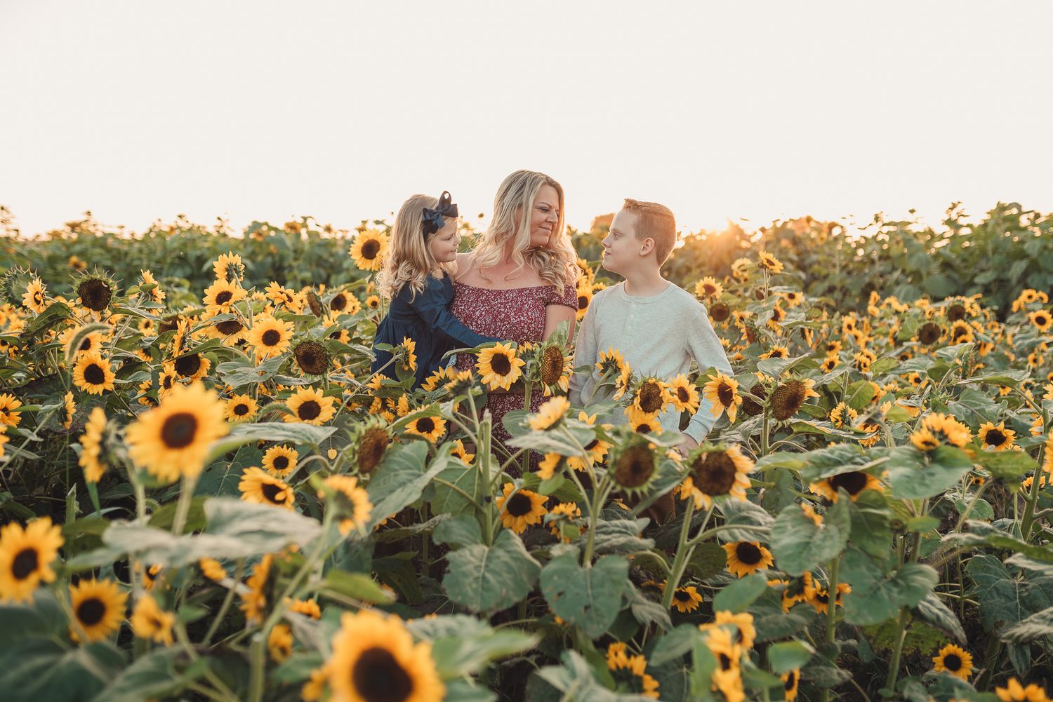 Three people share joyful moments together in a vibrant sunflower field at sunset.