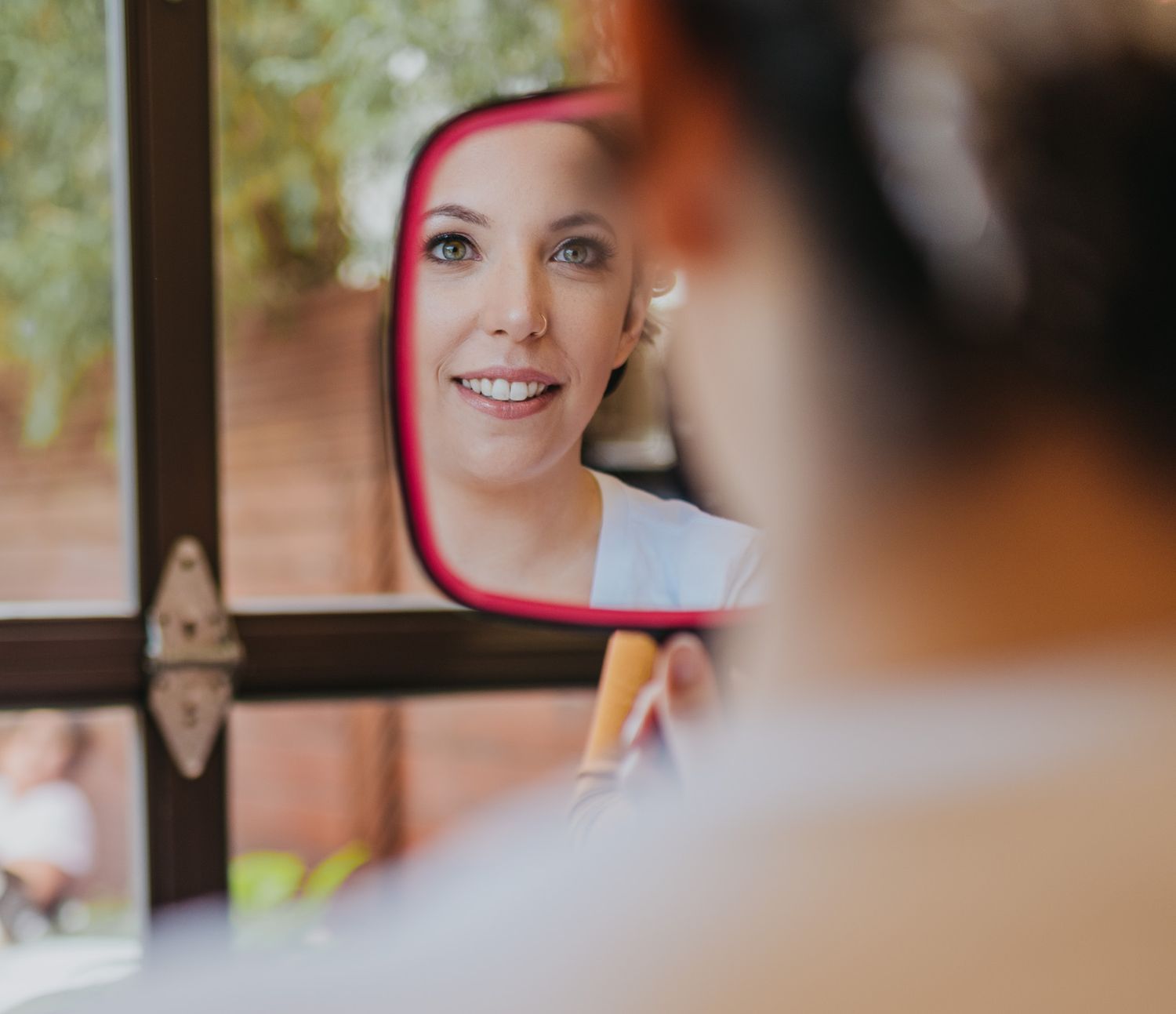 Creative reflection shot in car mirror during wedding day preparations.