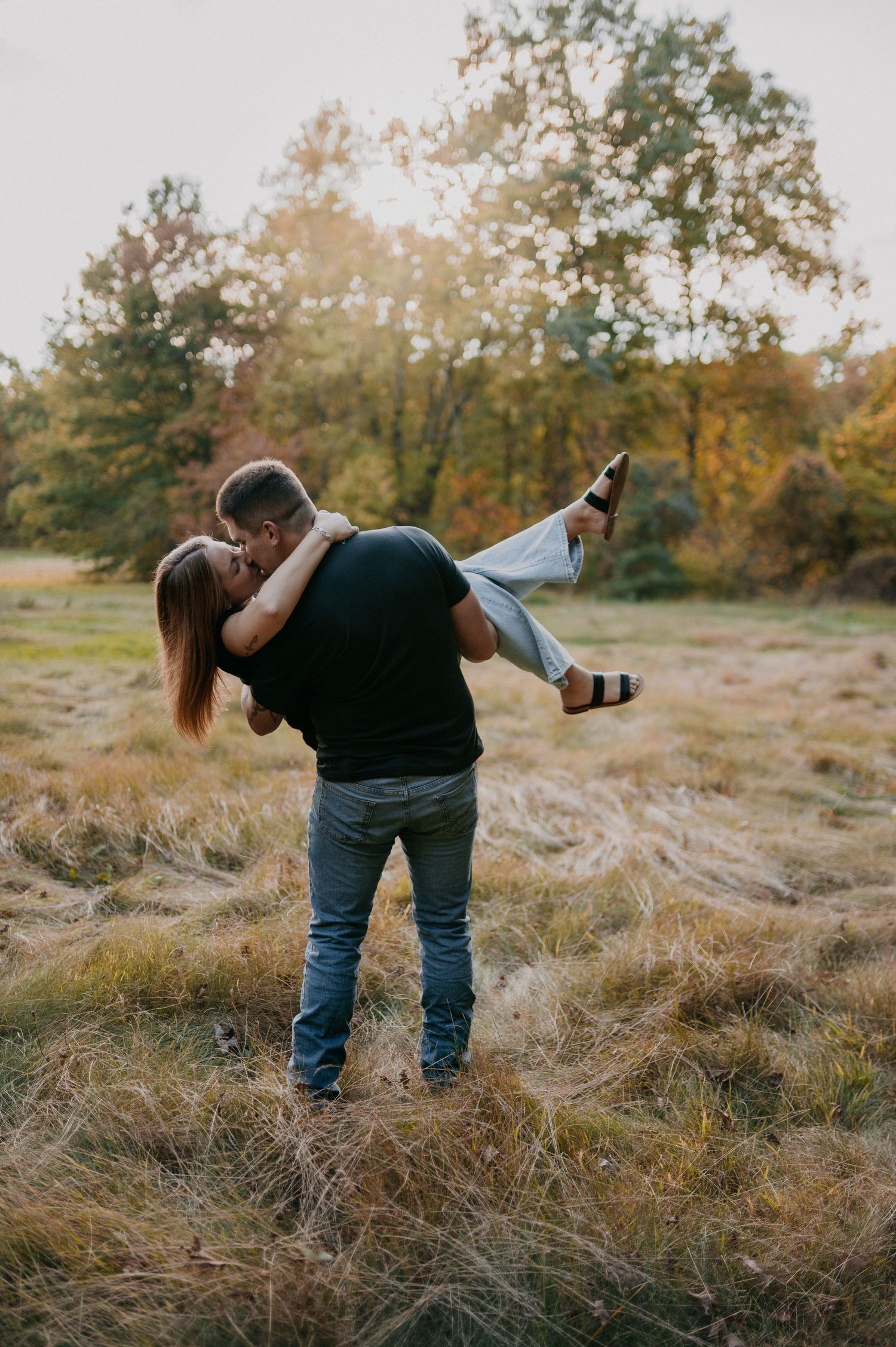 A couple dances together in a romantic dip pose amidst tall autumn grass during golden hour.