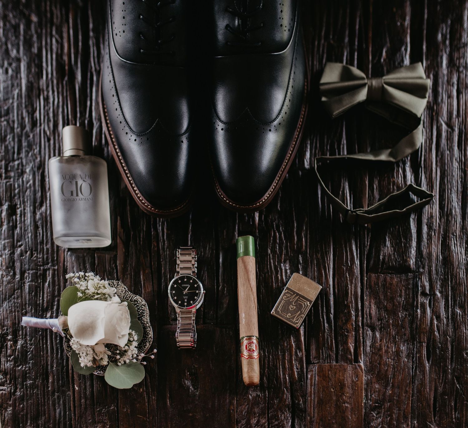 Wedding accessories and details arranged on dark wooden surface including shoes, watch, and rings.