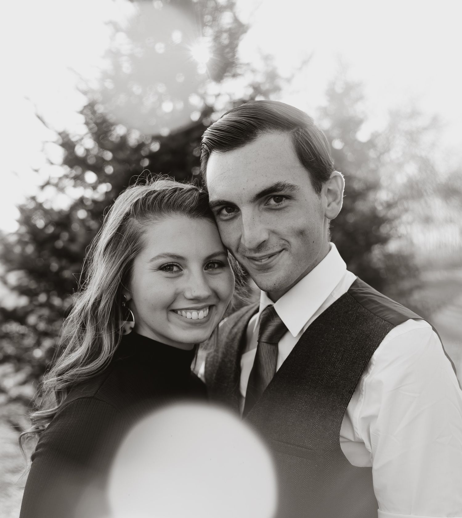Black and white romantic portrait of couple in formal attire with bokeh lighting effect.